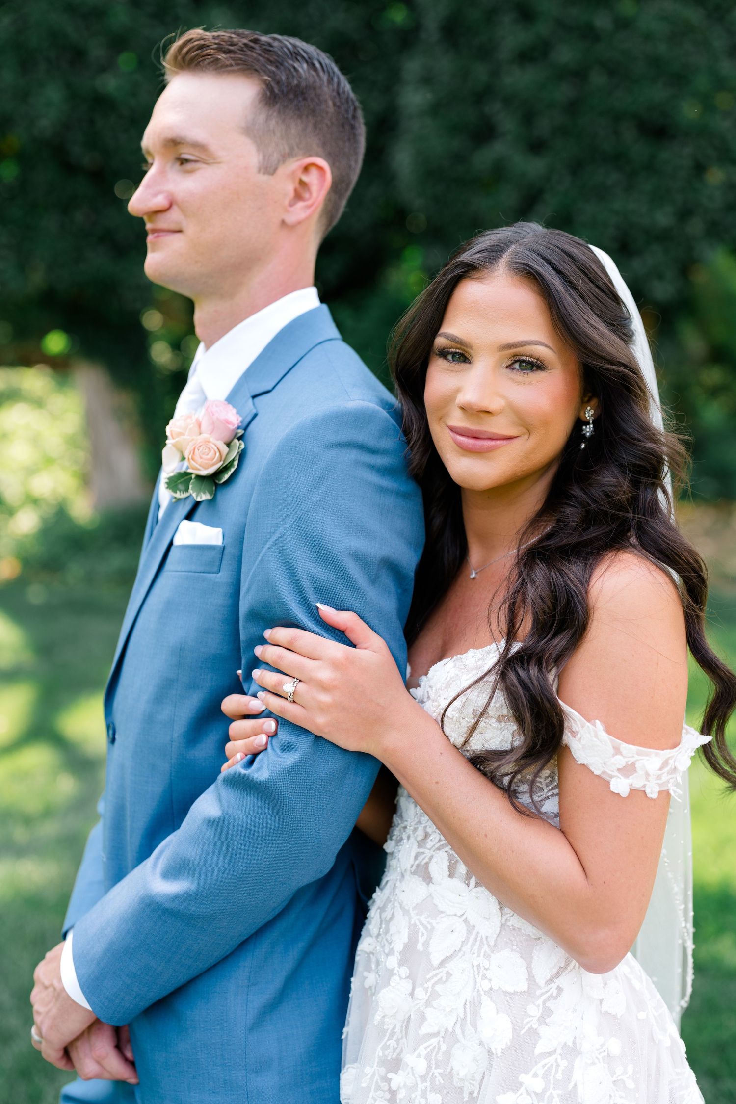 A bride and groom share intimate moments in a garden setting wearing a white lace gown and blue suit.