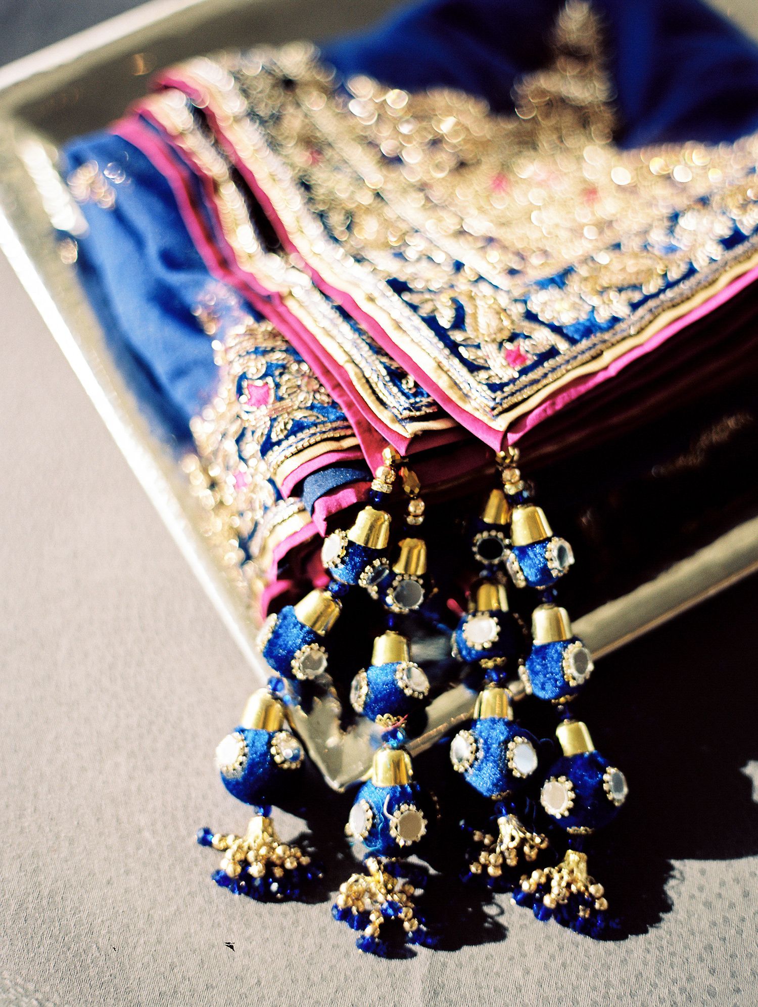 Ornate embroidered fabric with blue and pink tassels and beaded decorative trim details.