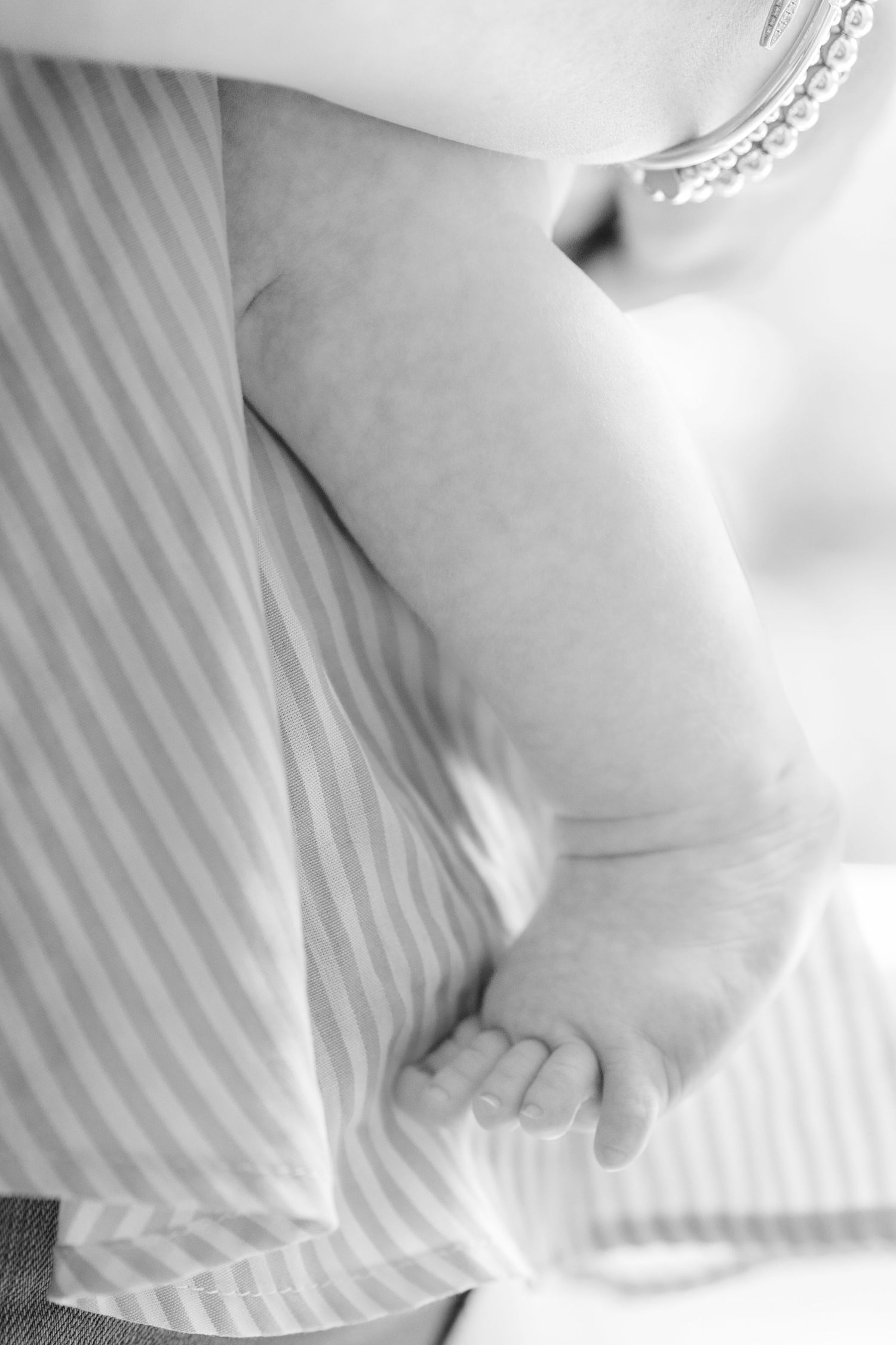Black and white close-up of a baby's tiny arm against striped fabric.
