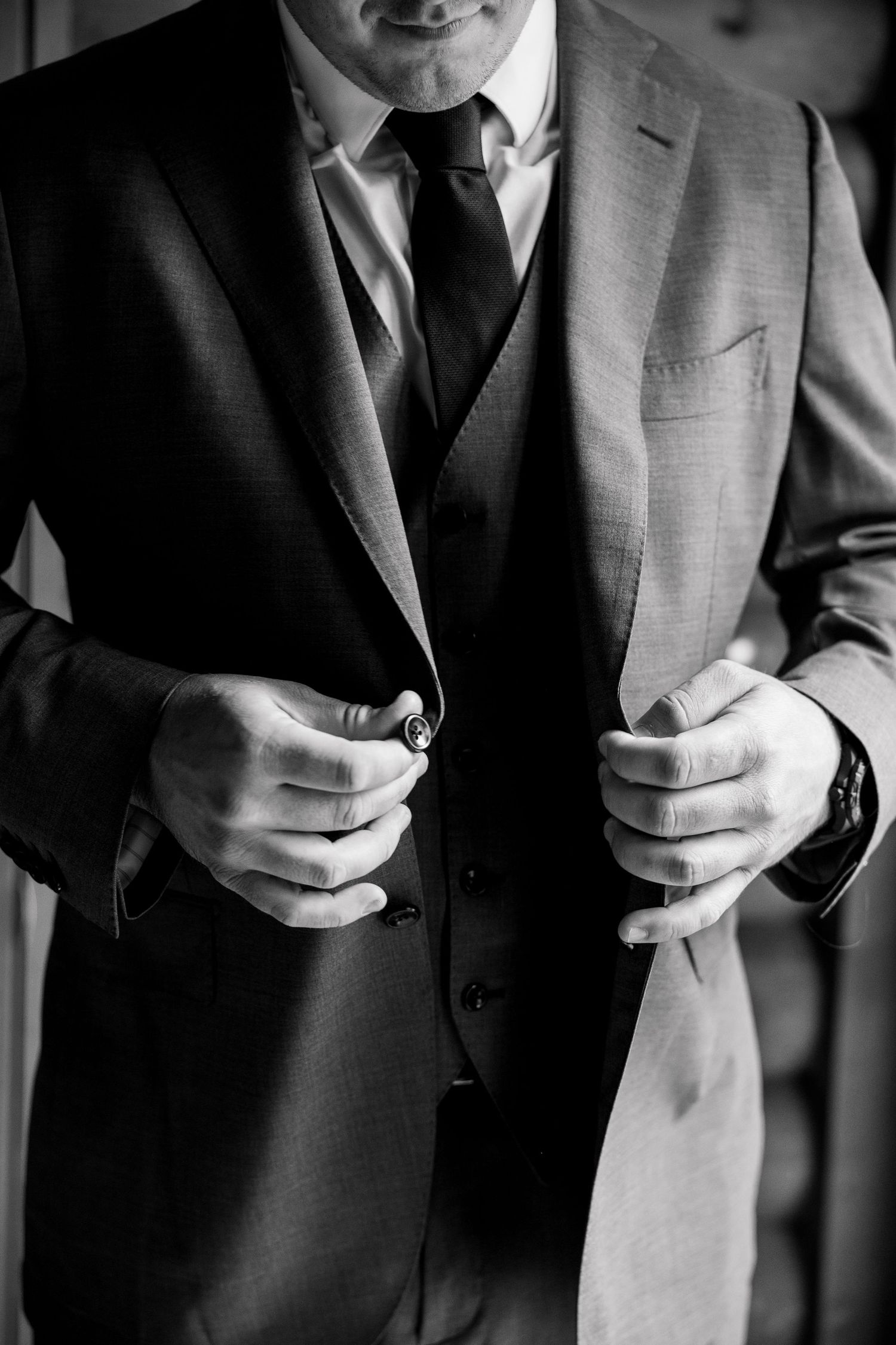 Close-up of a groom adjusting his suit jacket buttons before the wedding ceremony.