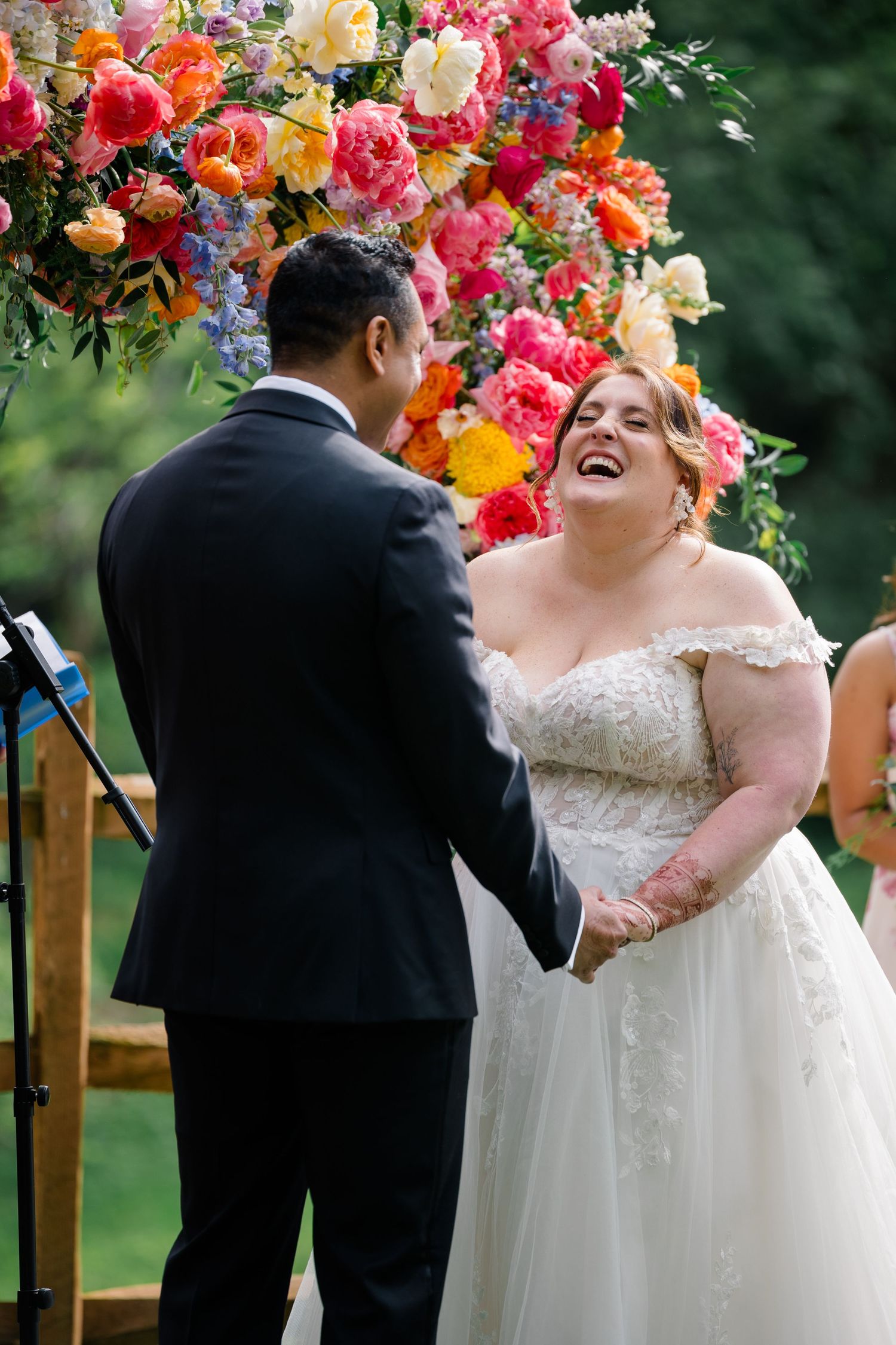 Joyful moment during wedding ceremony under vibrant floral arch decoration.