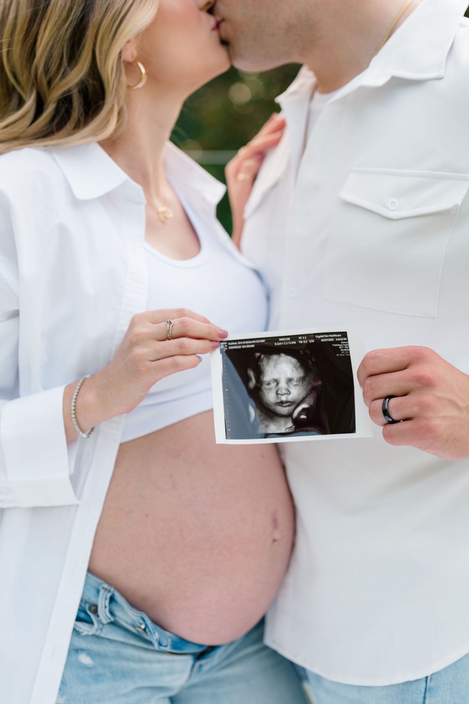 Outdoor maternity photoshoot showing couple holding ultrasound photos against a pregnant belly.