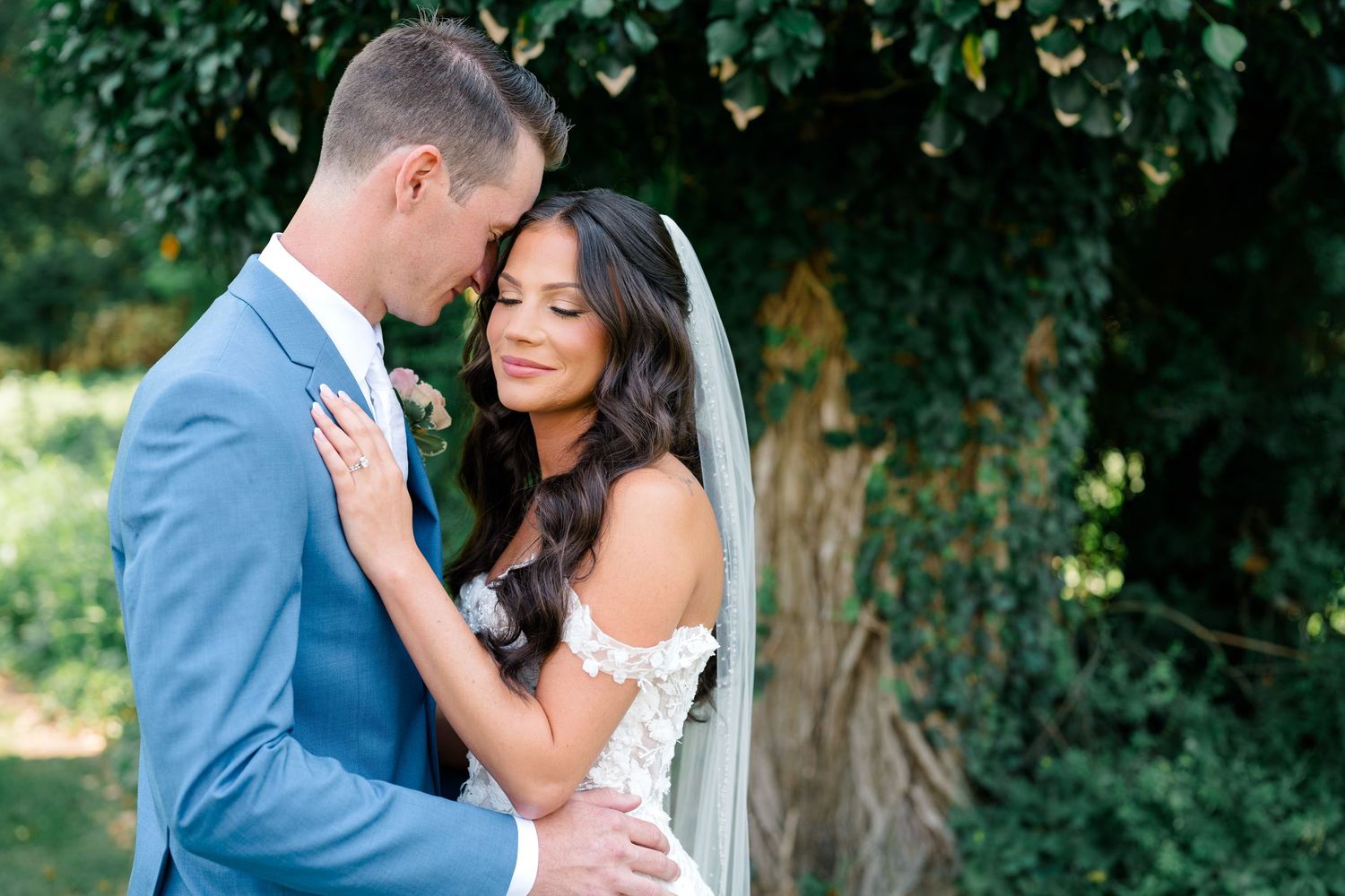 A romantic outdoor wedding portrait of a couple embracing against a green garden backdrop.