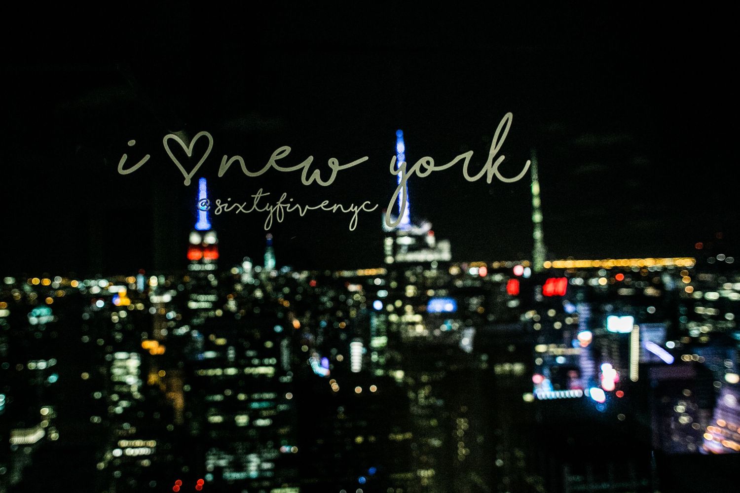 Blurred New York City skyline at night with neon text overlay against dark background.