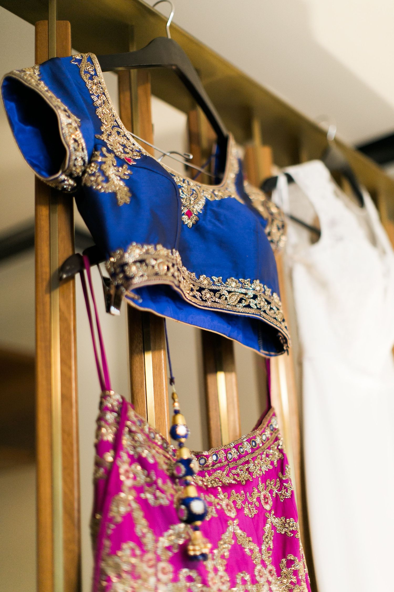 Traditional Indian ethnic wear with royal blue and pink lehengas featuring intricate gold embroidery hanging on display.