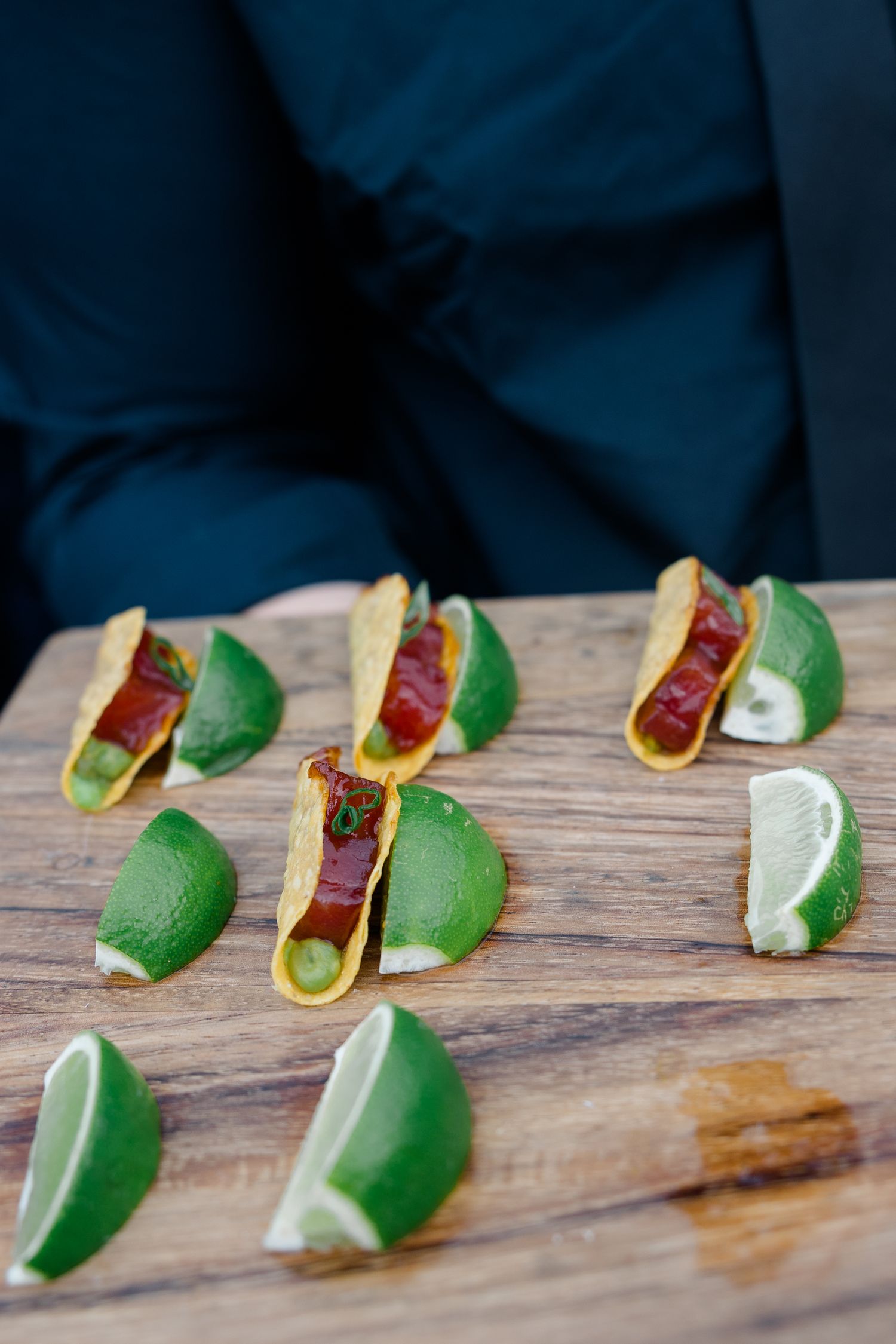 Mini tacos garnished with fresh lime wedges displayed on a wooden serving board.