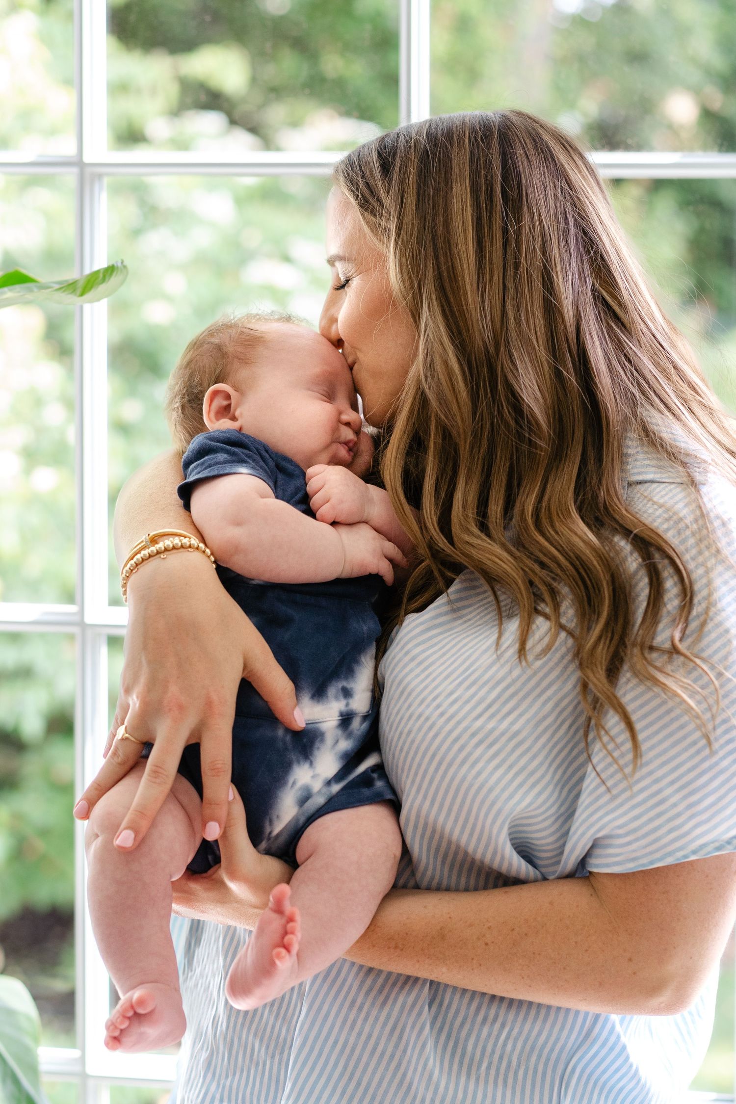 A tender moment captured by a window as a baby in navy clothing is held close.