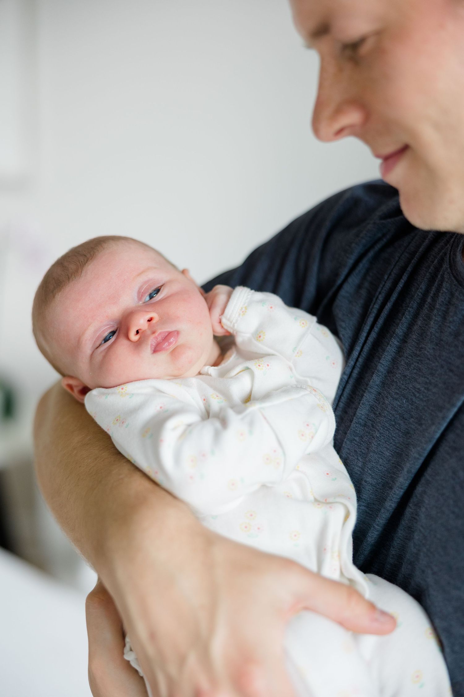 Baby in white onesie rests against caregiver wearing dark shirt.
