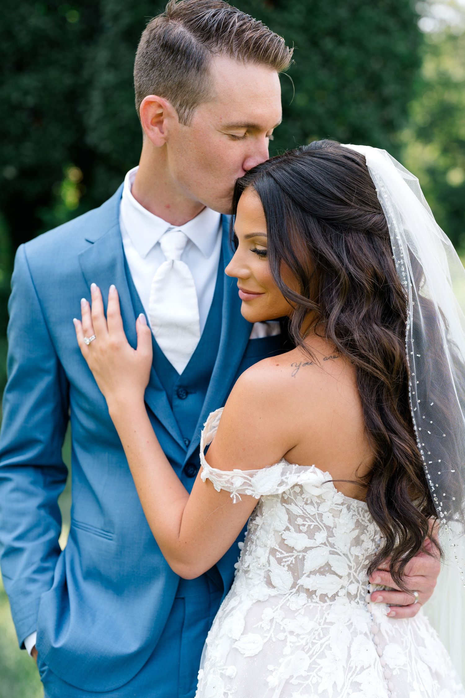 Romantic wedding couple portraits featuring a blue suit and white lace dress in an outdoor garden setting.