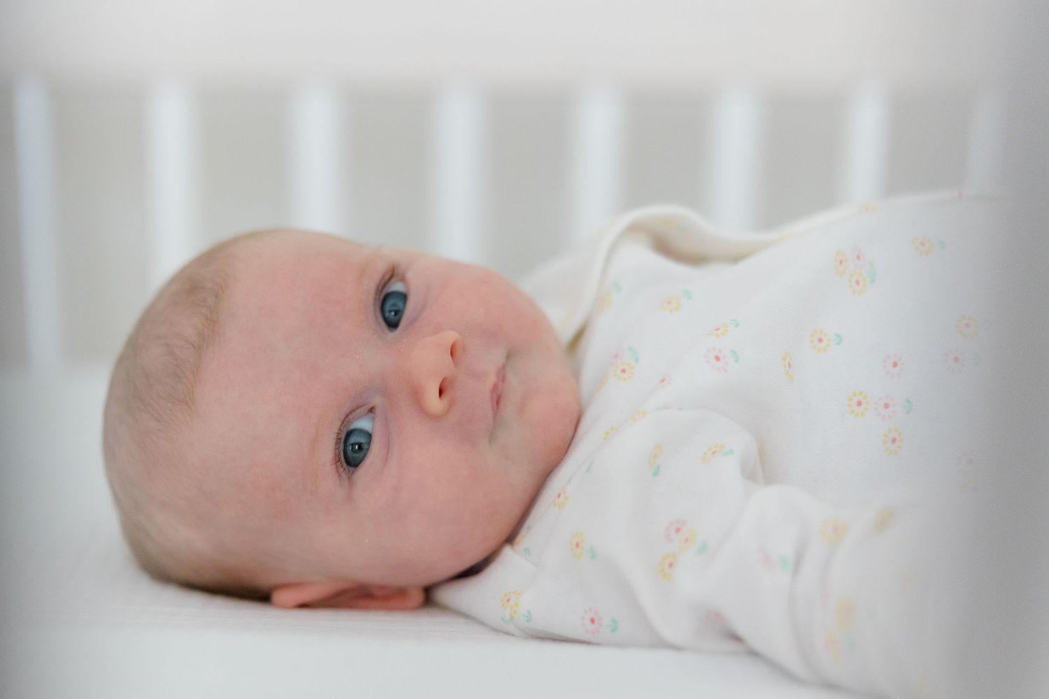 Close up of newborn baby with bright blue eyes lying on white bedding.