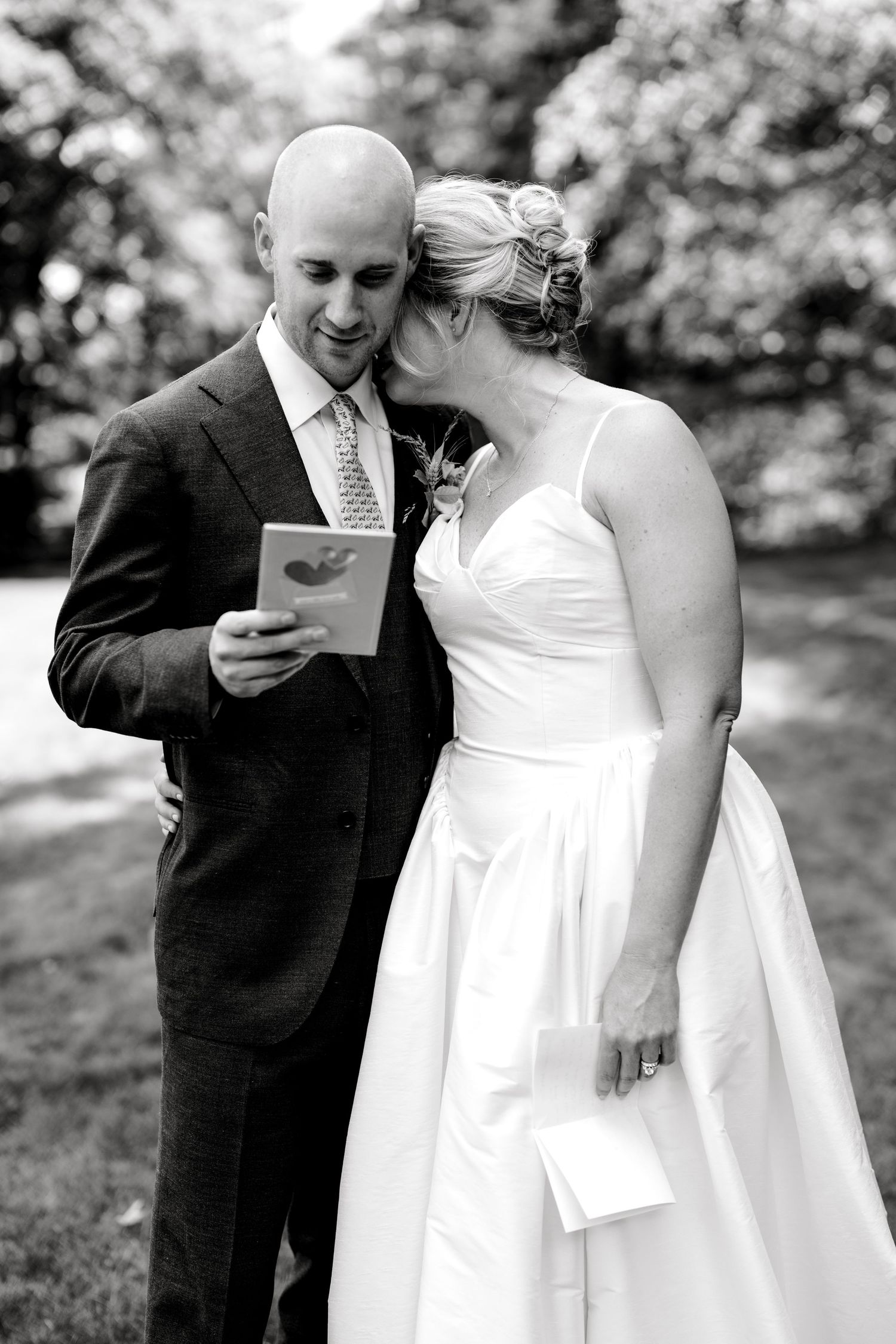 Black and white photo of a bride and groom reading heartfelt letters to each other outdoors.