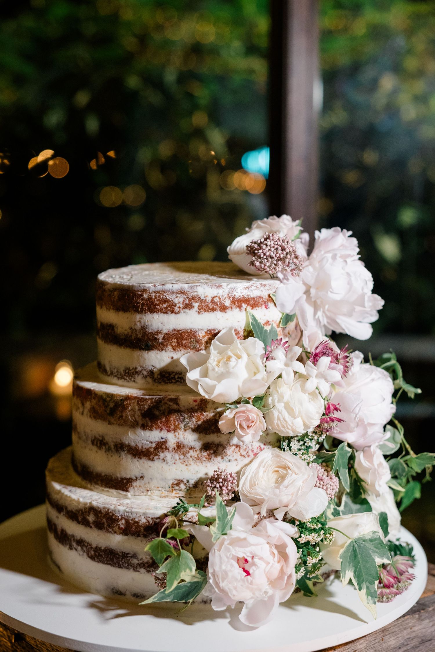 A rustic naked wedding cake decorated with fresh pink and white flowers.