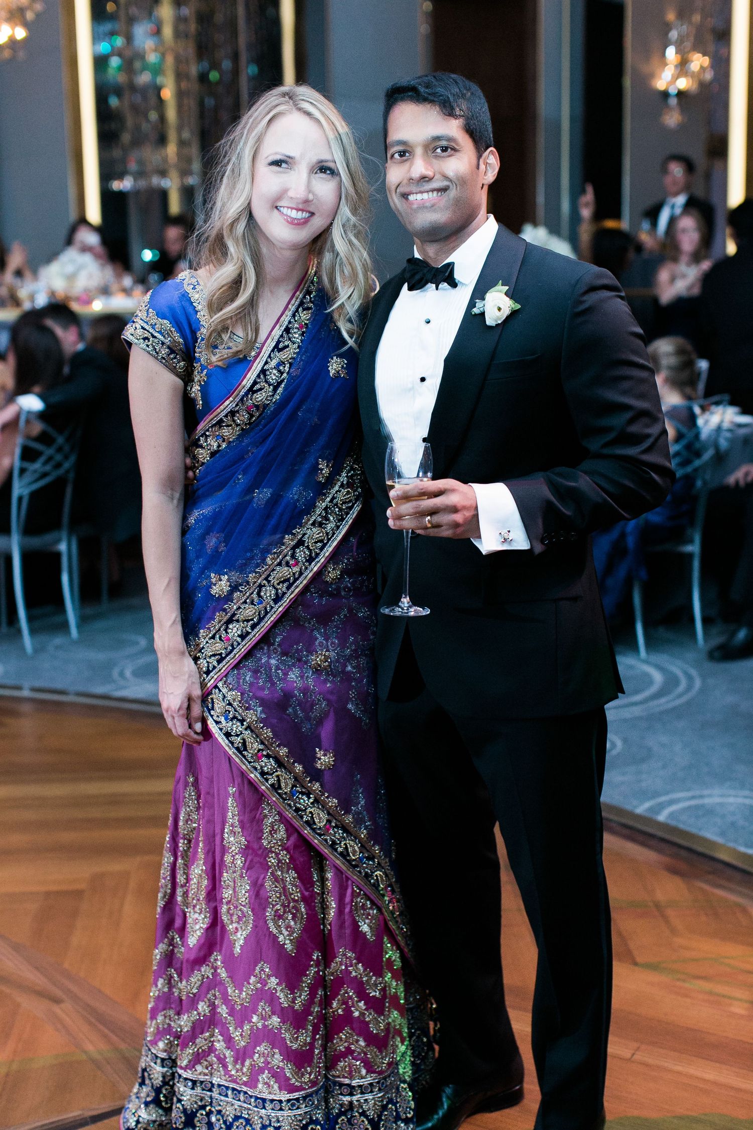 A formal event with guests in elegant attire including a blue and purple sari and black tuxedo.