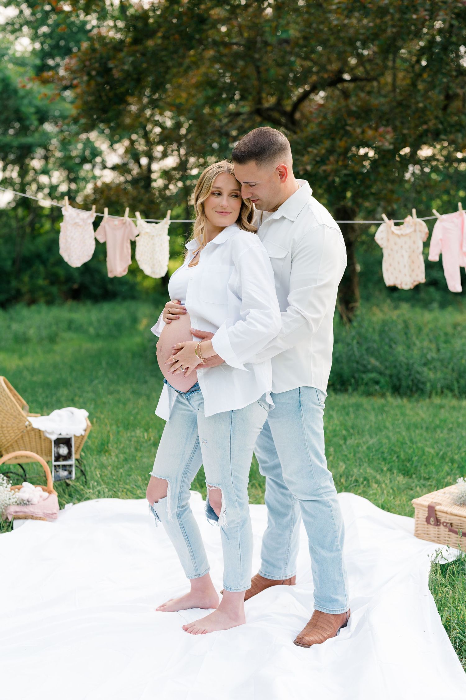 Outdoor maternity scene with white backdrop and baby clothing decor on clothesline.