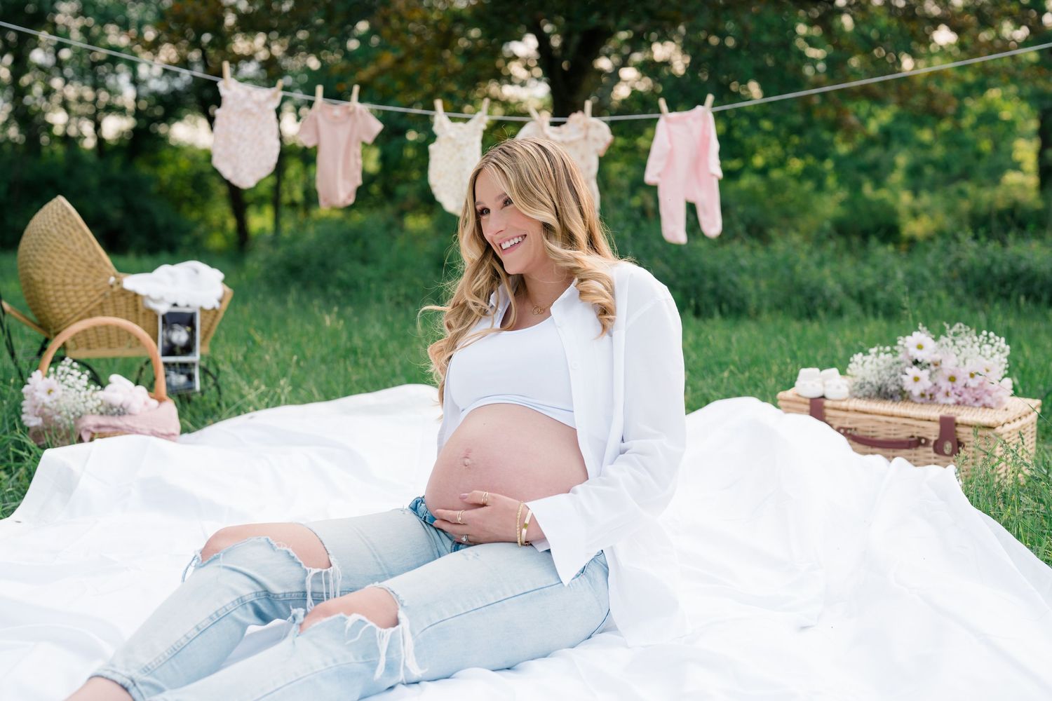 Couple lounging on white blanket outdoors with baby clothes hanging on clothesline in background.
