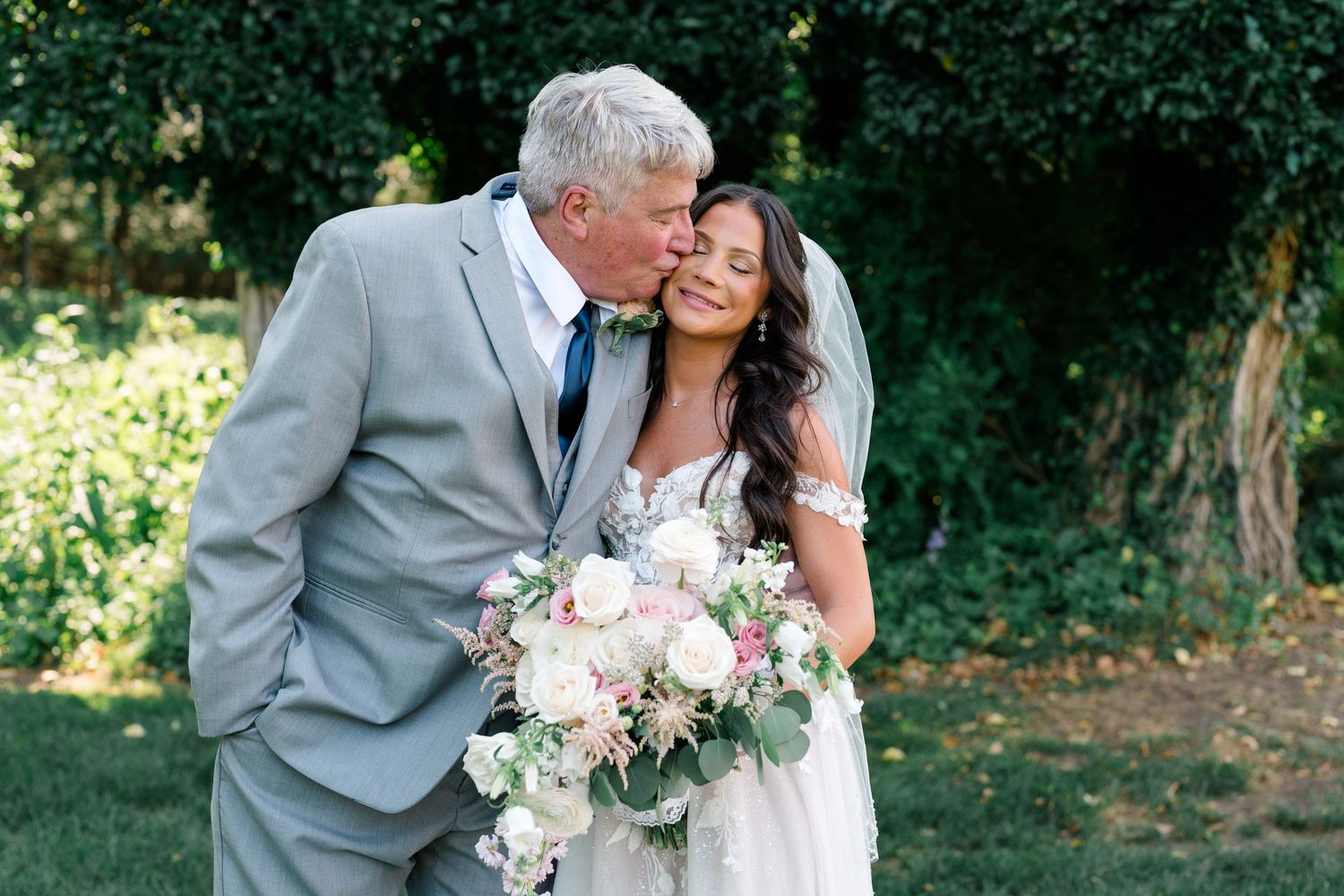 A touching moment captured between newlyweds with a pink and white floral bouquet in garden setting.