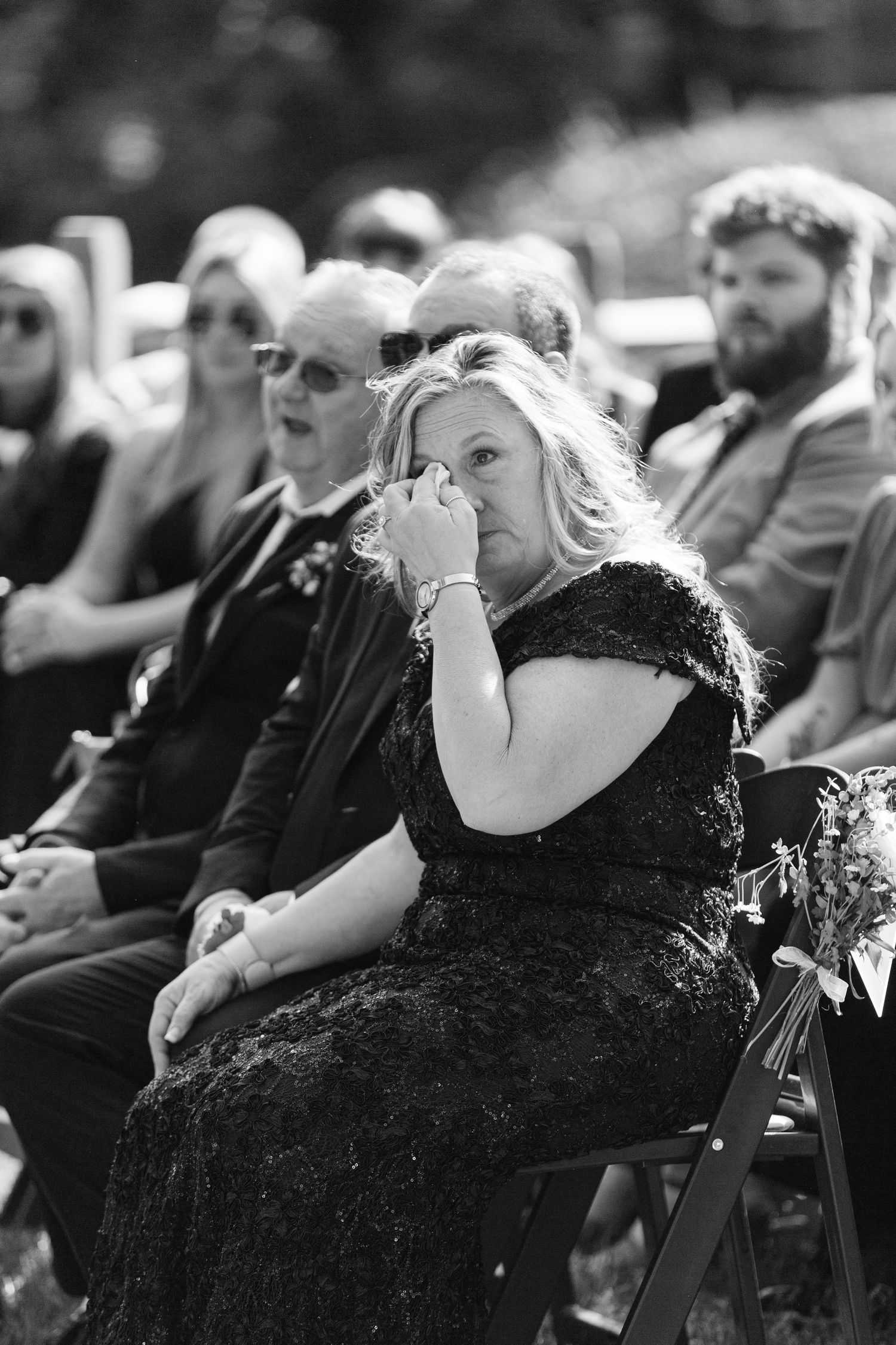 Wedding guests dressed in black formal attire sitting in rows during an outdoor ceremony.