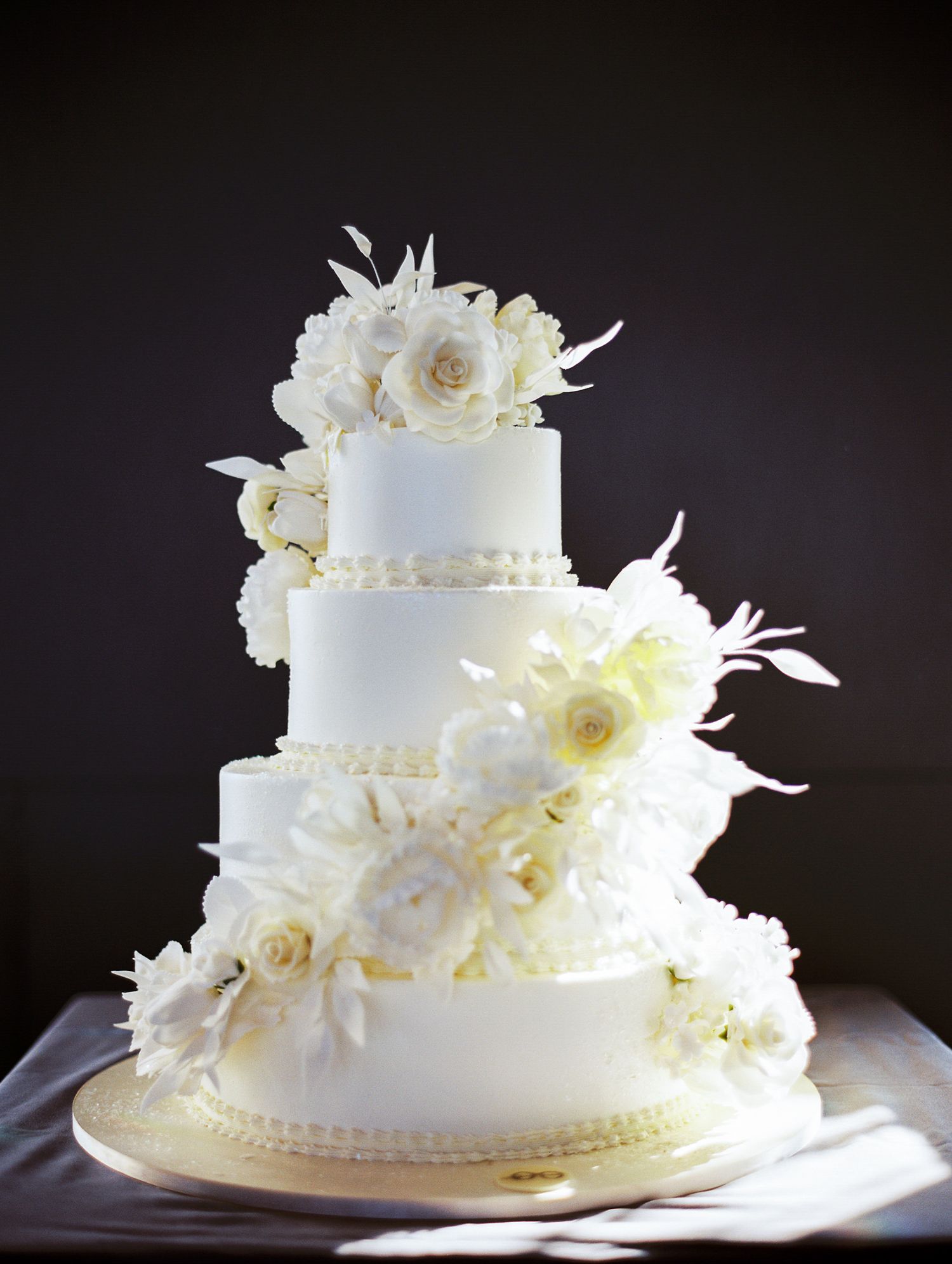 Elegant four-tier white wedding cake decorated with fresh white flowers and feathers.
