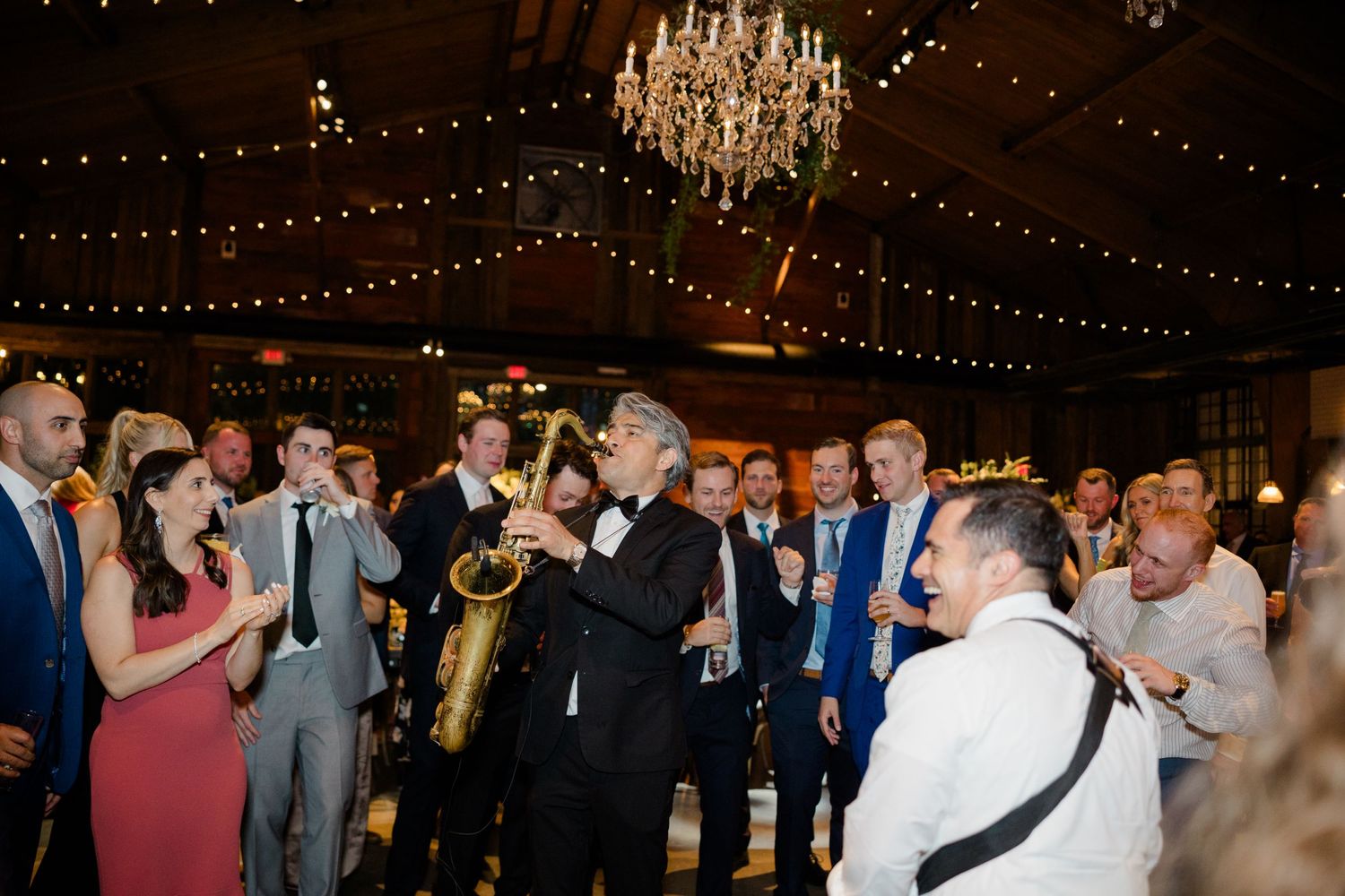 Wedding celebration in an elegant ballroom with crystal chandelier and string lights overhead.