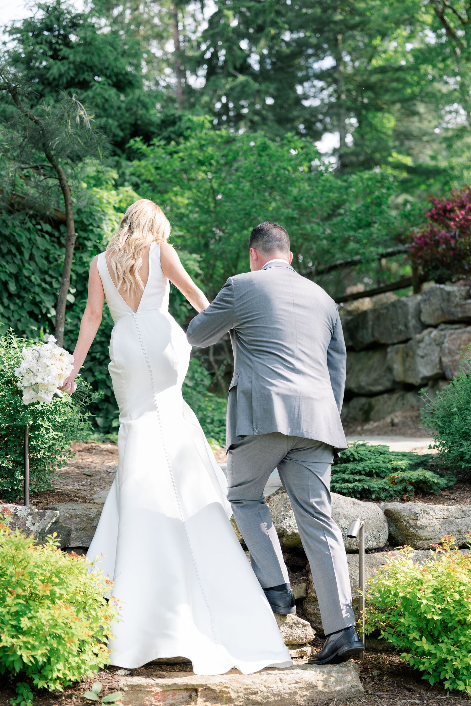 A couple walking up stone garden steps with the bride's white dress flowing behind them.