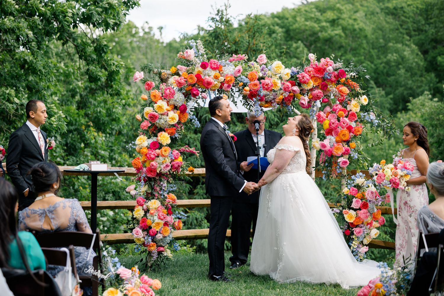 Outdoor wedding celebration with bright coral floral arch arrangements.