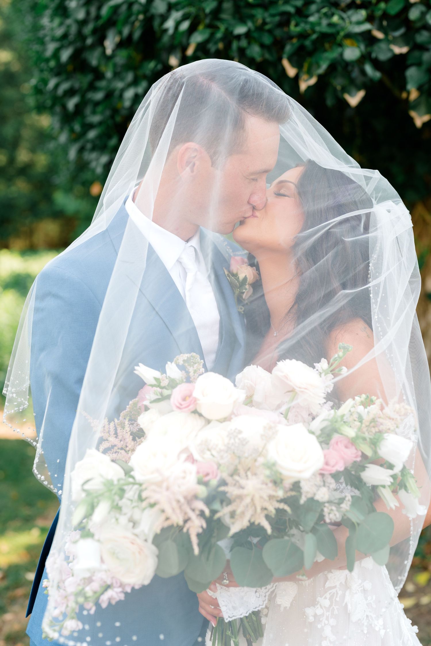 Romantic wedding photo under veil with pink and white bouquet.