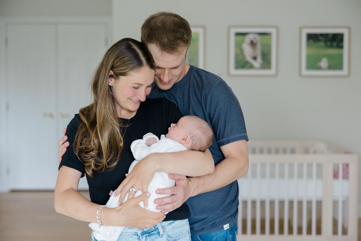 A couple in a nursery room shares a tender moment with their newborn baby while standing near a white crib.