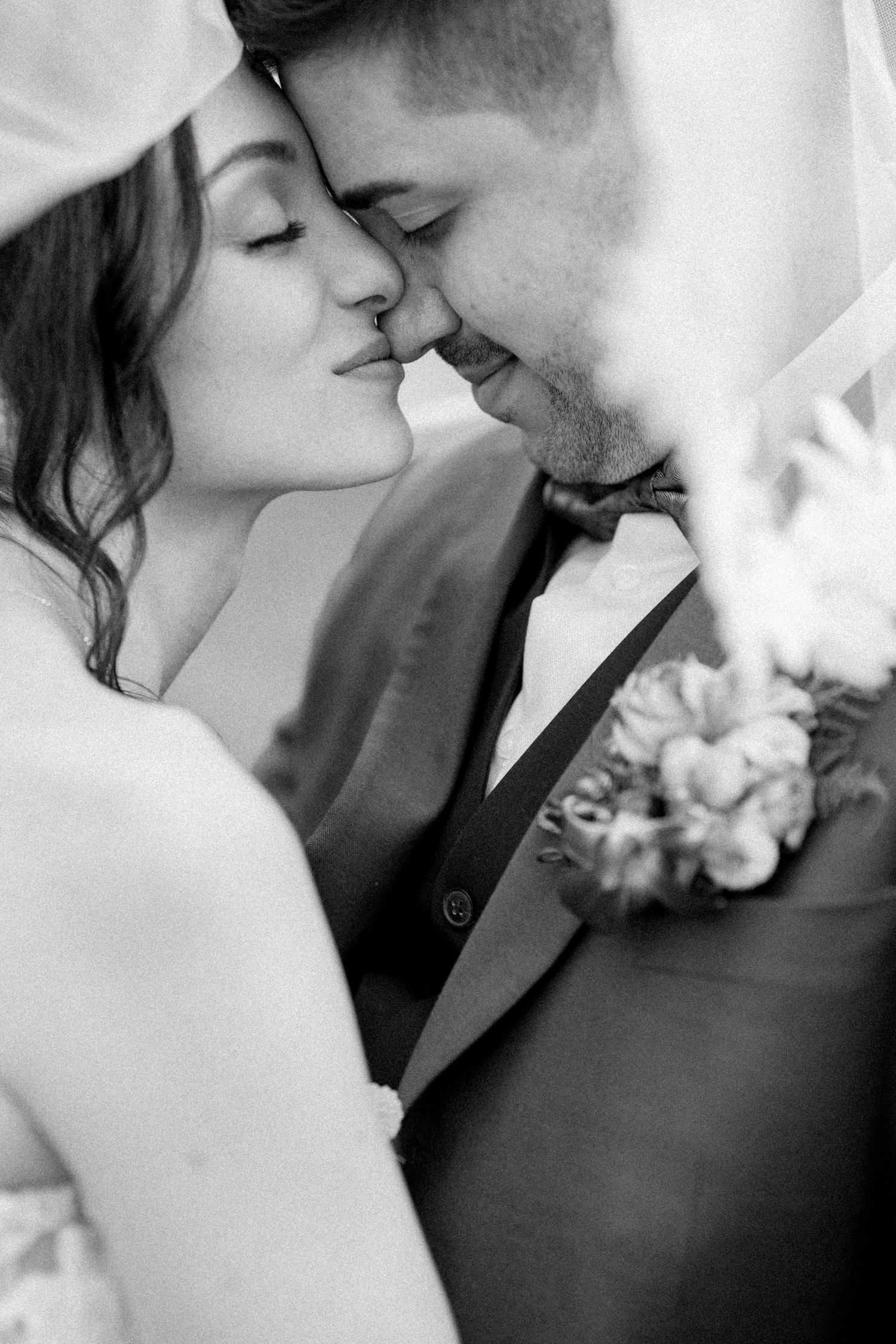 Black and white romantic wedding photo showing intimate moment between couple with groom wearing boutonniere.