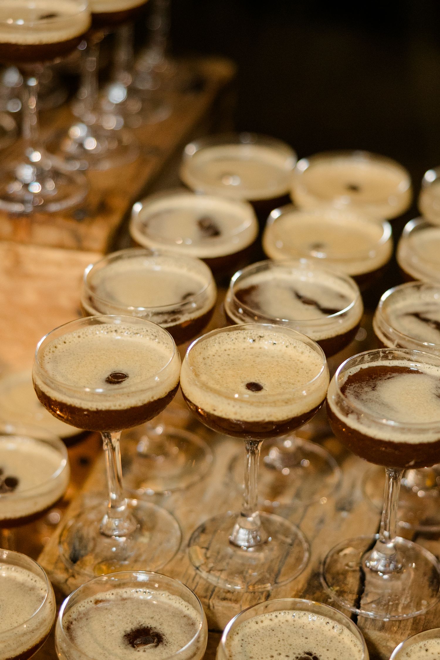 Row of espresso martini cocktails with frothy tops lined up on a bar.