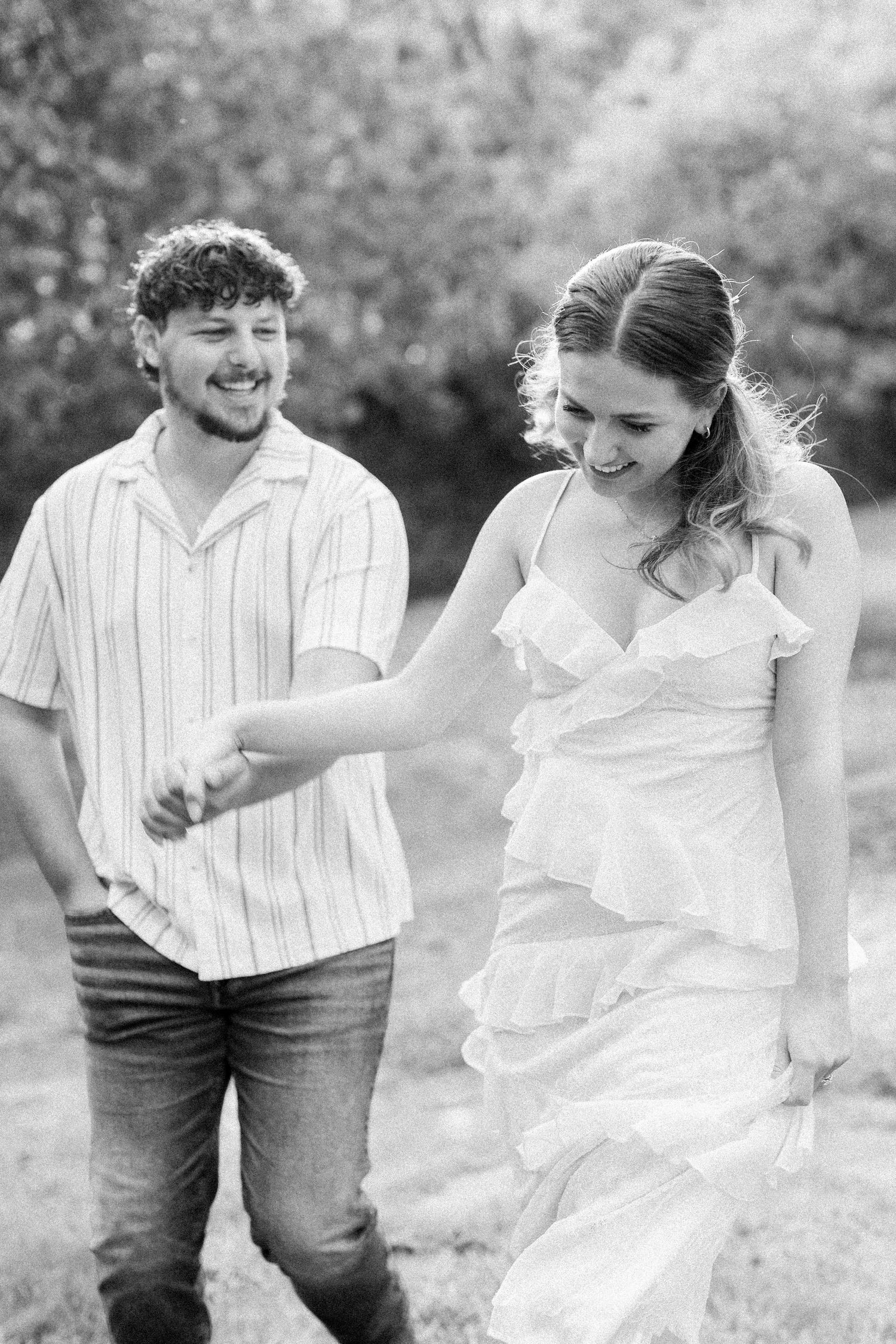 Black and white photo of a smiling couple holding hands and walking outdoors during an engagement session.