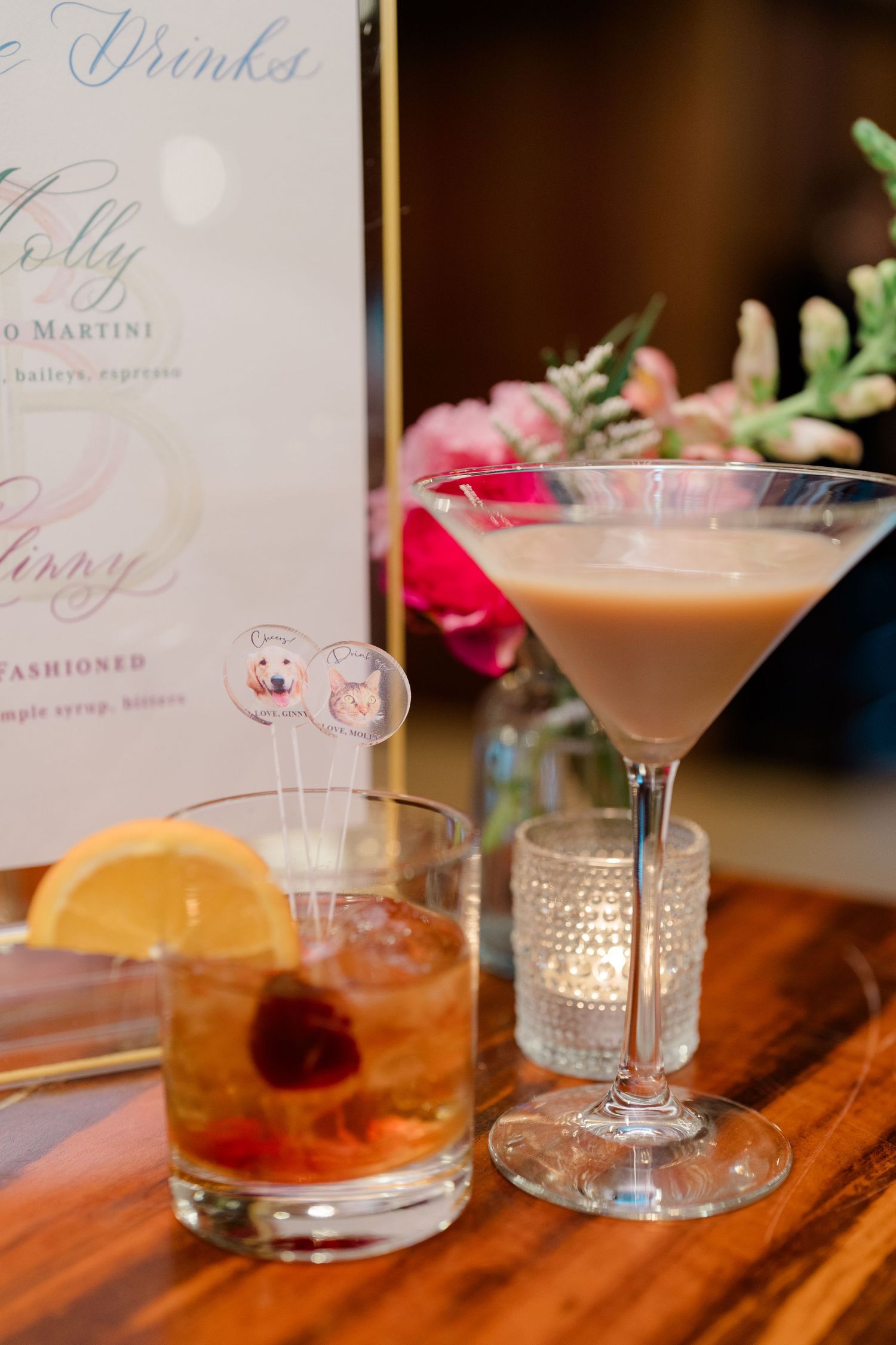 Two elegant cocktails on wooden table with drinks menu and floral decor.
