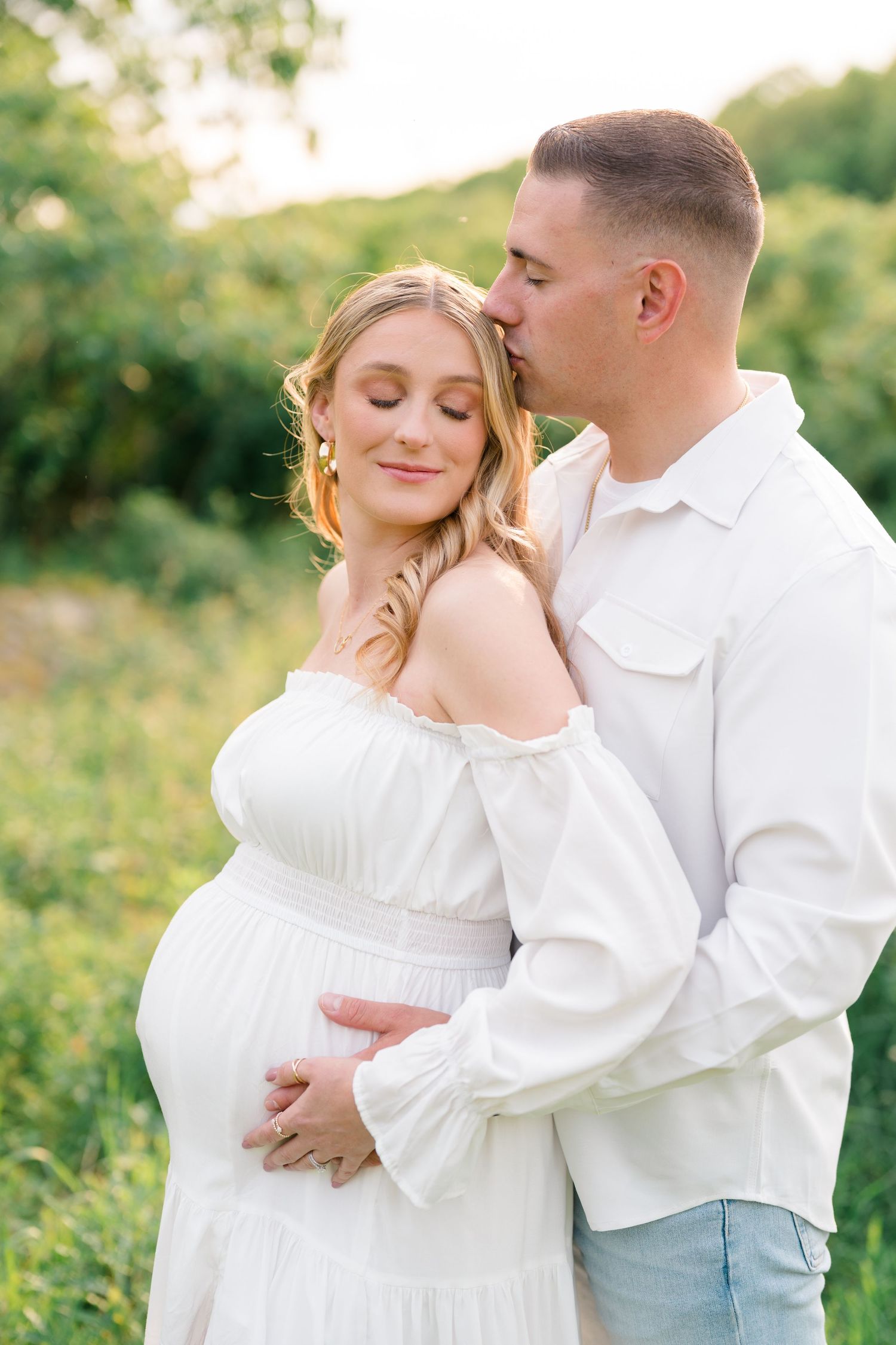 Intimate maternity portraits captured in soft evening light with couple in white clothing.