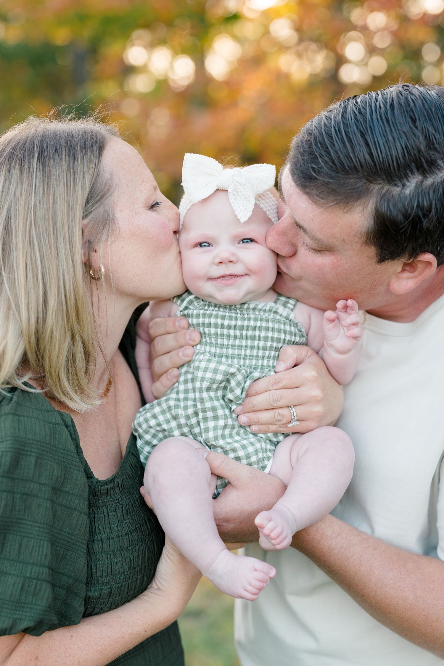 Sweet family portrait series showing parents kissing baby in green checkered outfit against blurred autumn background.