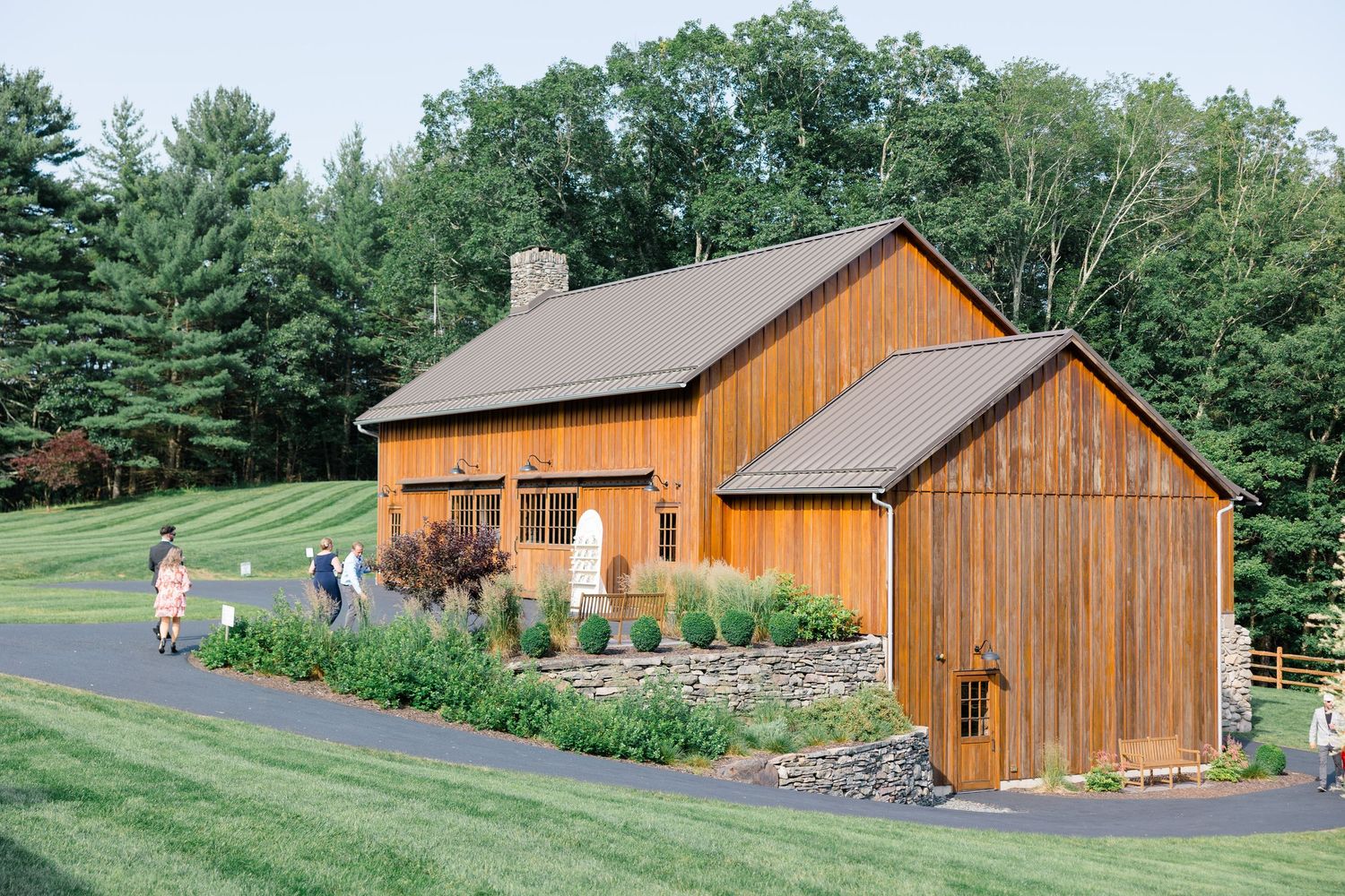 Rustic wooden barn venue with landscaped garden path surrounded by evergreen trees.