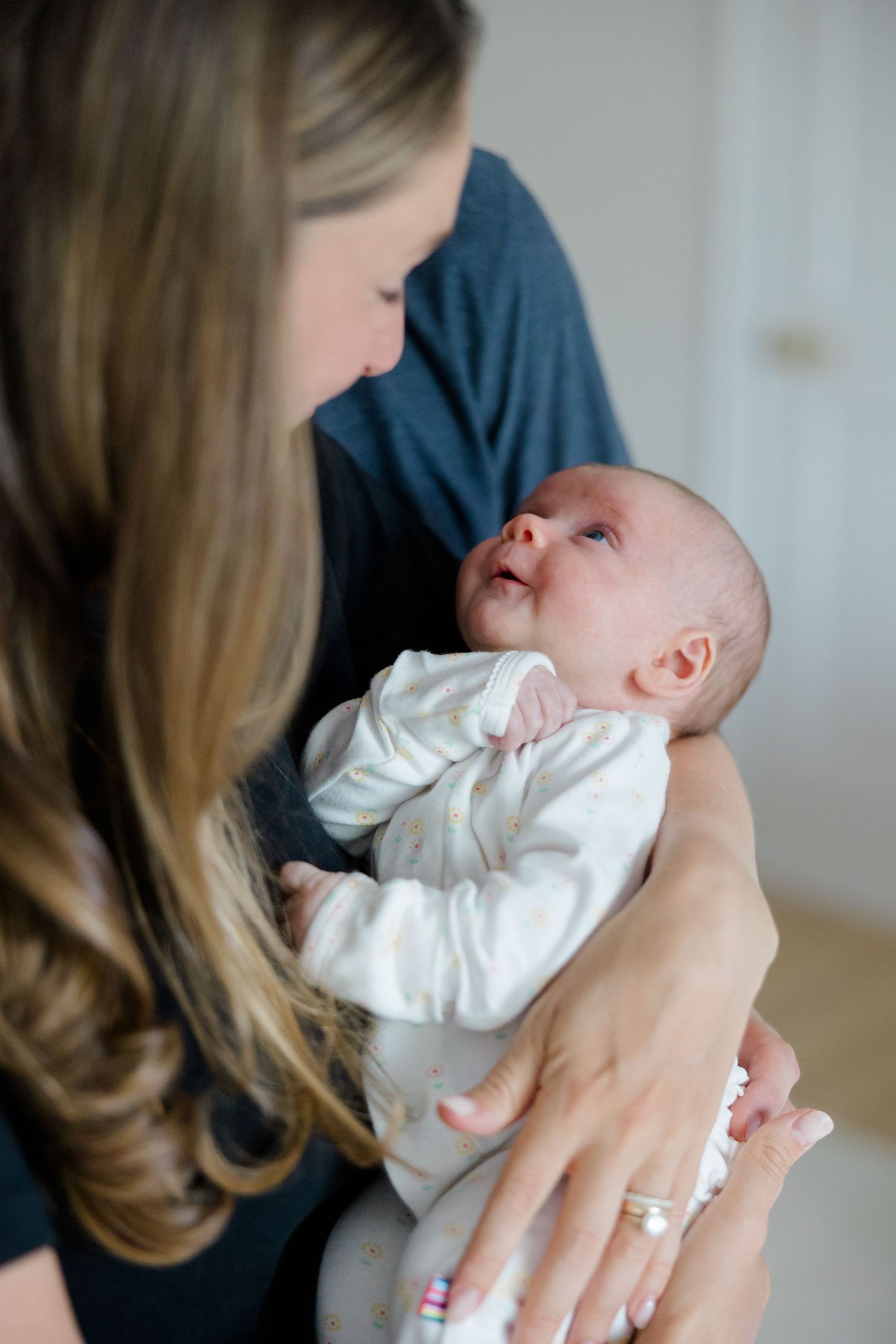 An intimate close-up of a baby in white clothing being cradled while gazing upward.