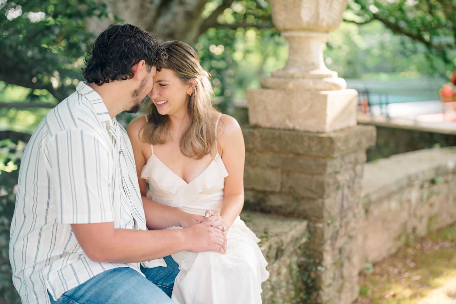 Couple sitting closely together on stone steps, sharing an intimate moment outdoors surrounded by lush greenery.