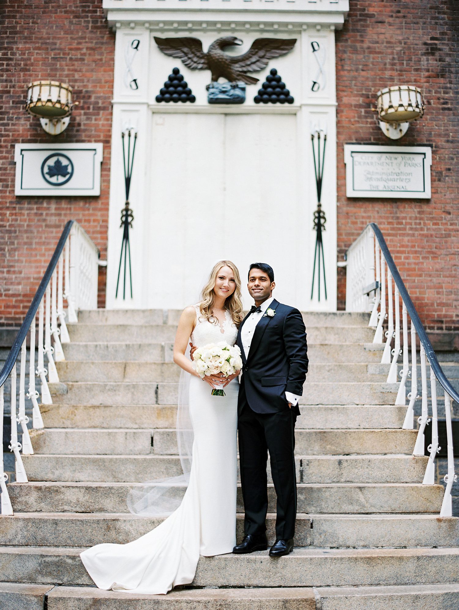 Newlyweds pose on elegant brick building steps with decorative railings and architectural details.