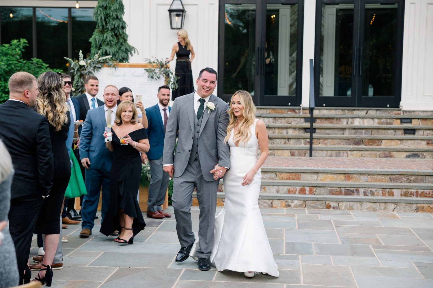 Wedding party exits venue onto stone patio during daytime celebration.