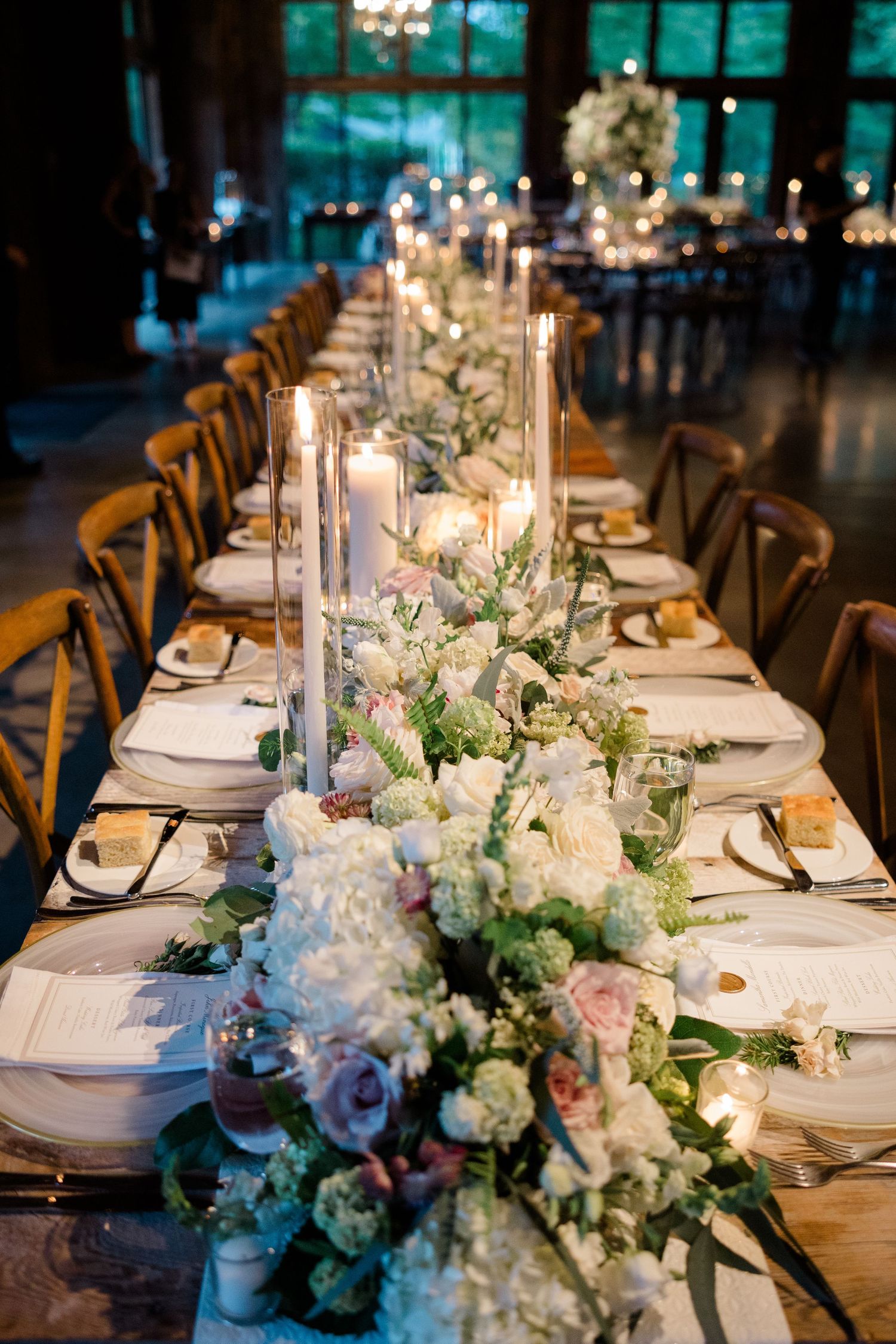 Elegant wedding reception table decorated with white floral arrangements and glowing candles in a rustic venue.