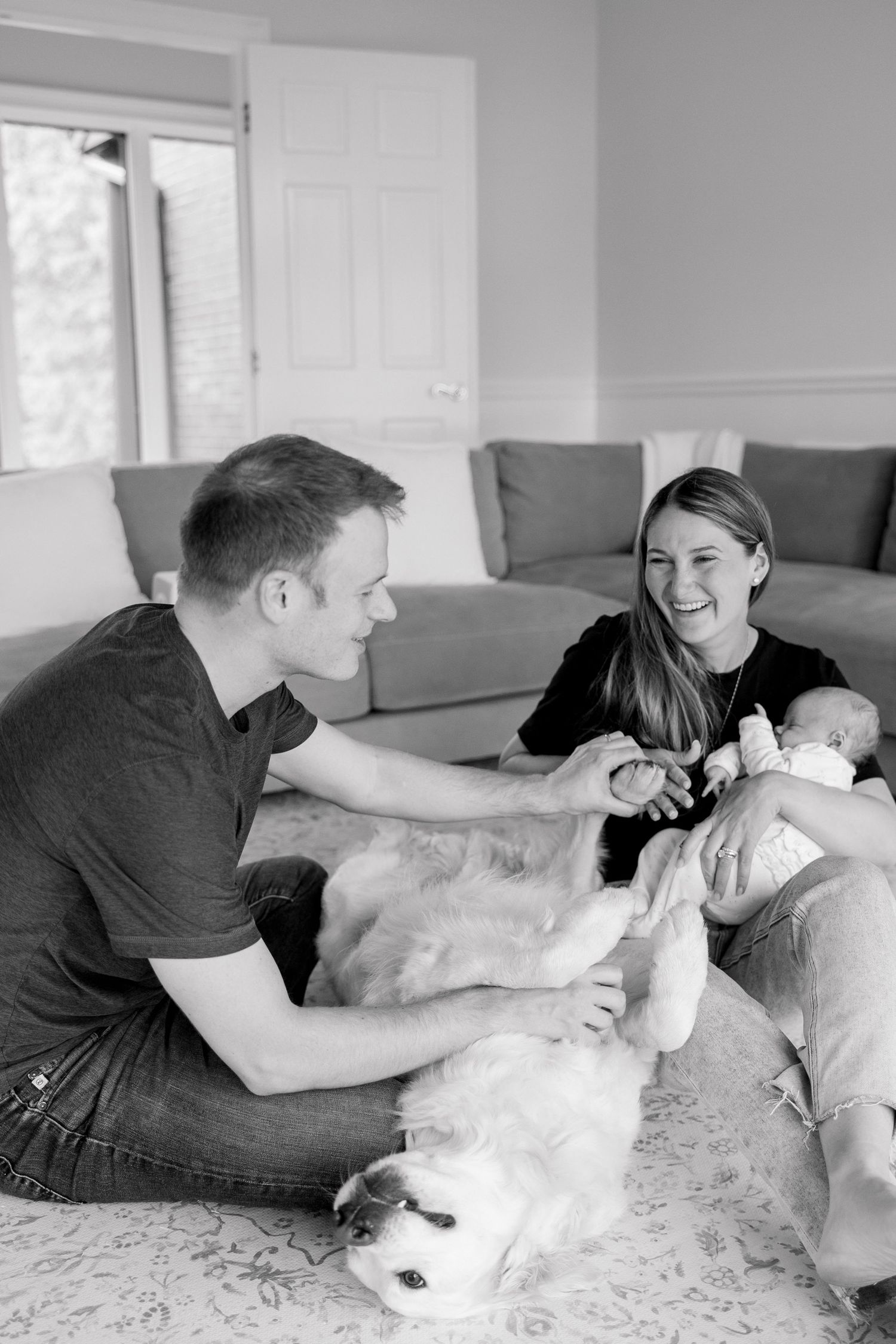 Black and white photo of family playing with dog on living room floor.