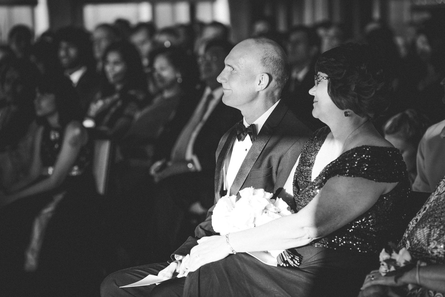 Black and white image of formally dressed people seated at an elegant event in a theater or concert hall.
