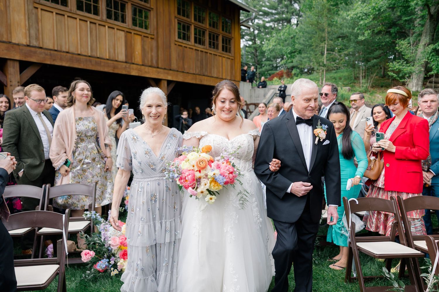Outdoor wedding ceremony with guests seated under wooden pavilion.