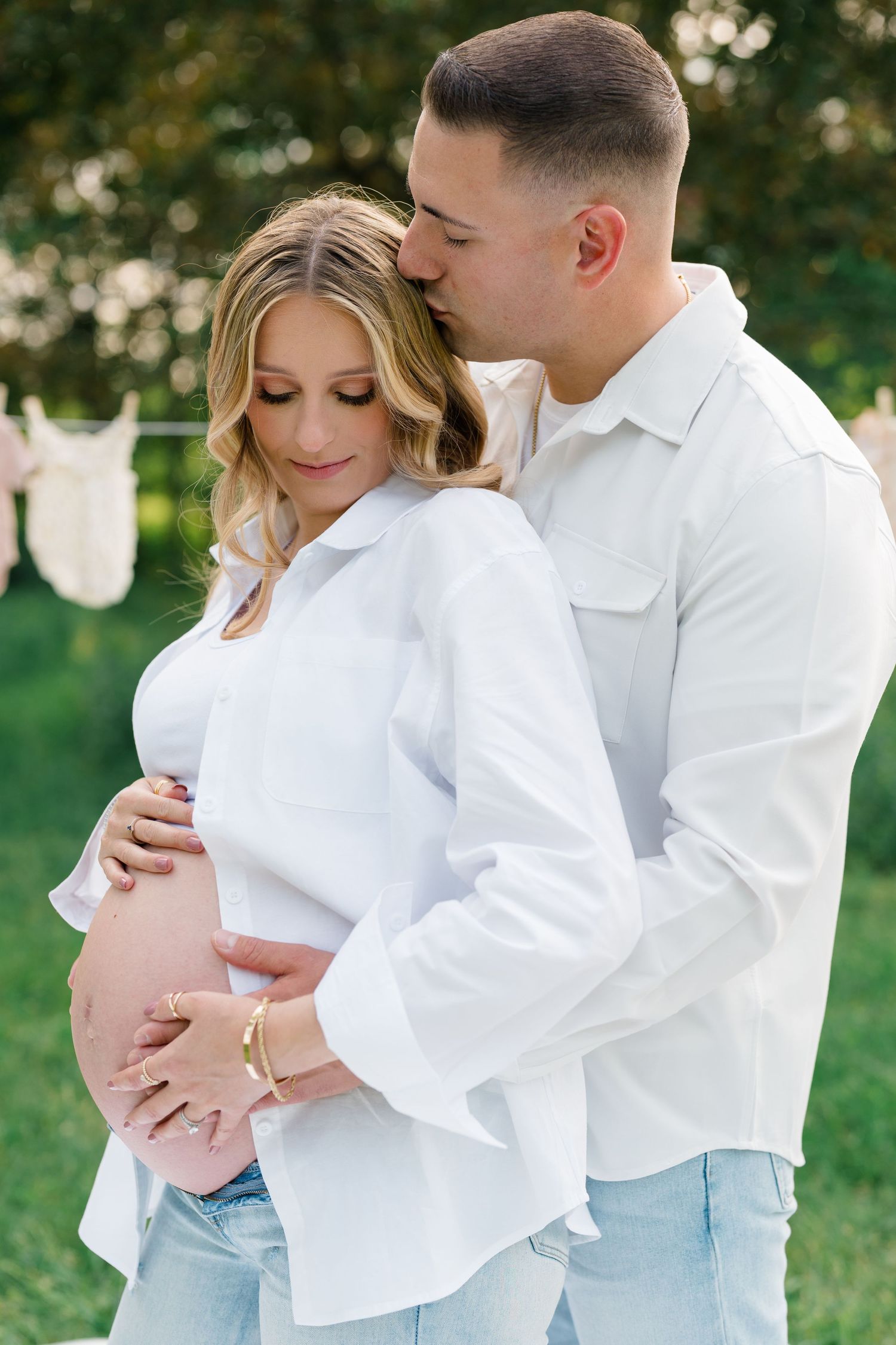 Couple in coordinating white outfits share tender moments during outdoor maternity session.