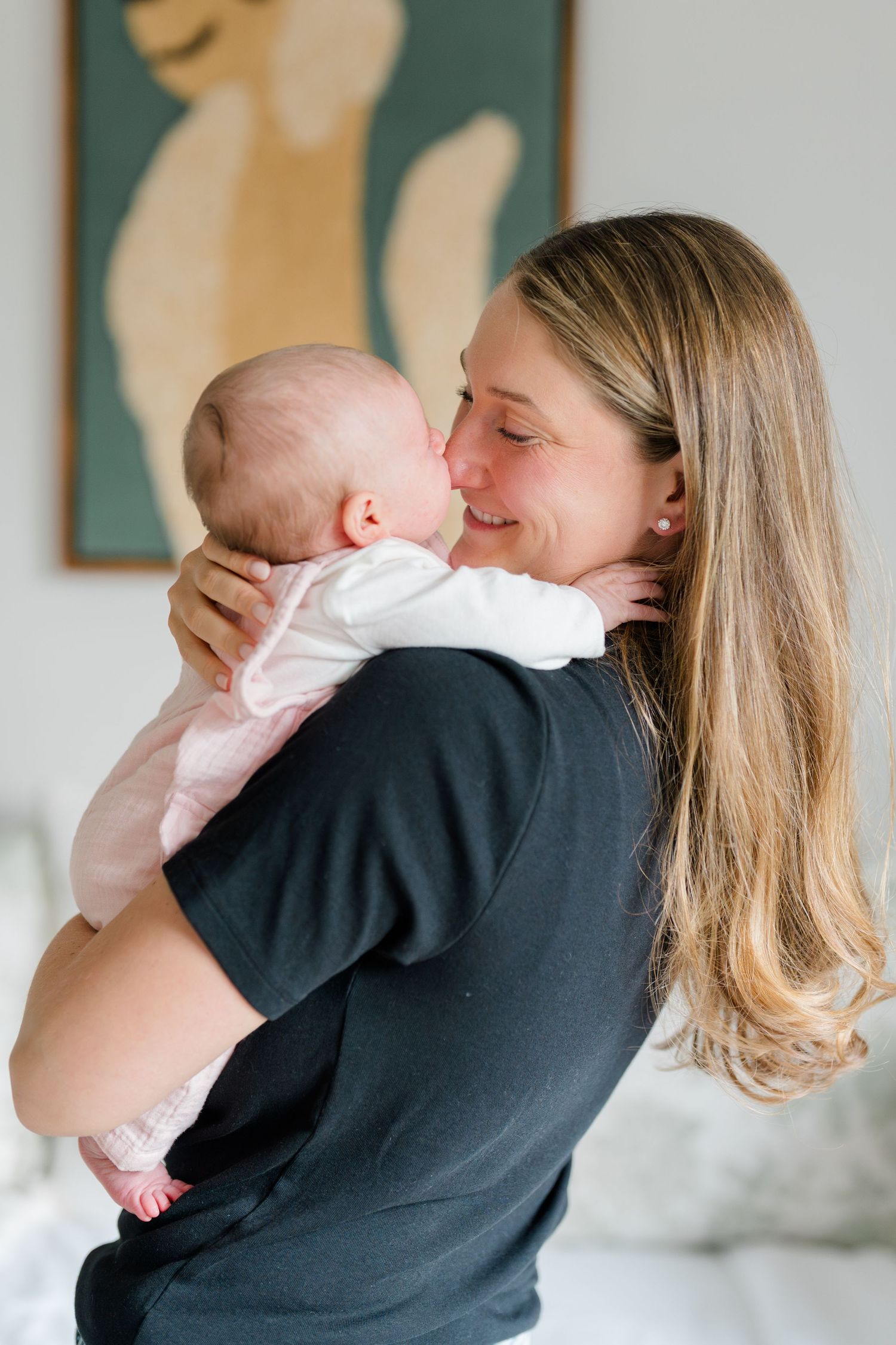 A tender moment between parent and infant as they embrace in a soft-lit room with minimalist artwork in the background.