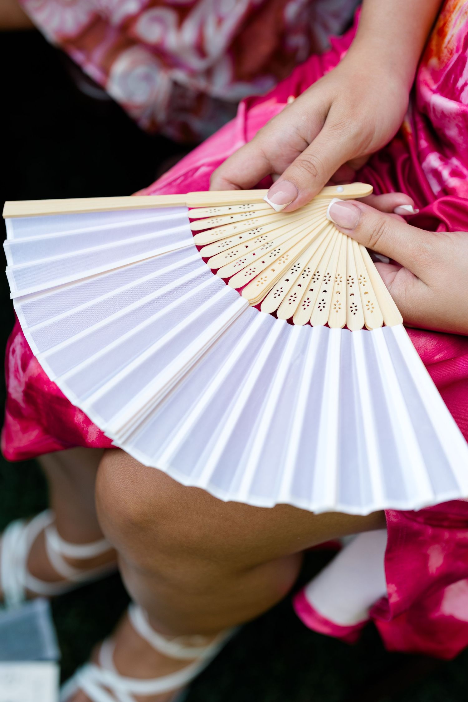White paper hand fan with wooden details shown against pink fabric.