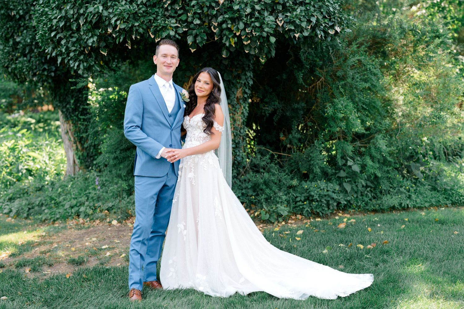 A romantic outdoor photo session showing a couple in wedding attire surrounded by lush green foliage.