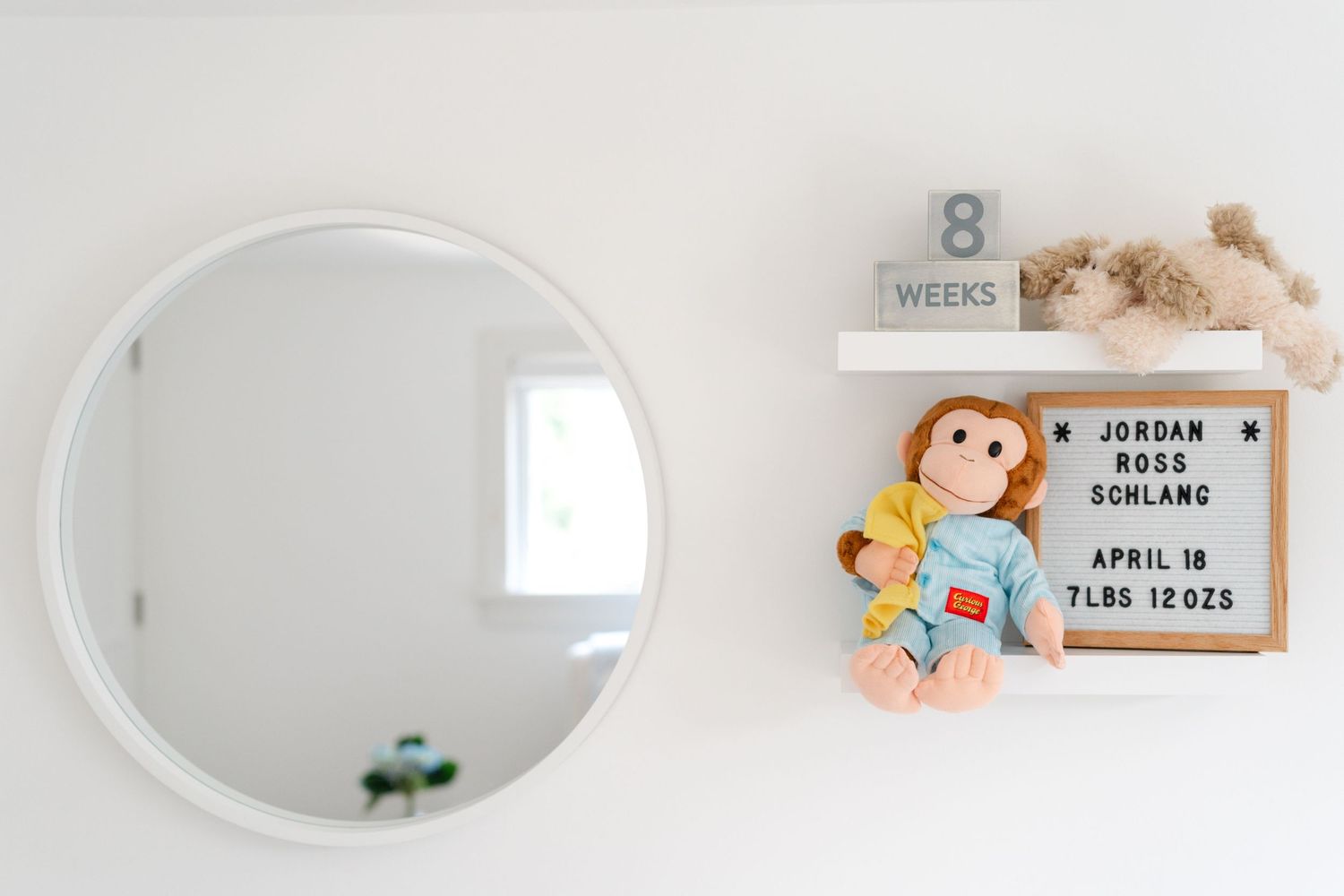 Simple round mirror and decorative monkey letterboard with number 8 displayed on white nursery wall.
