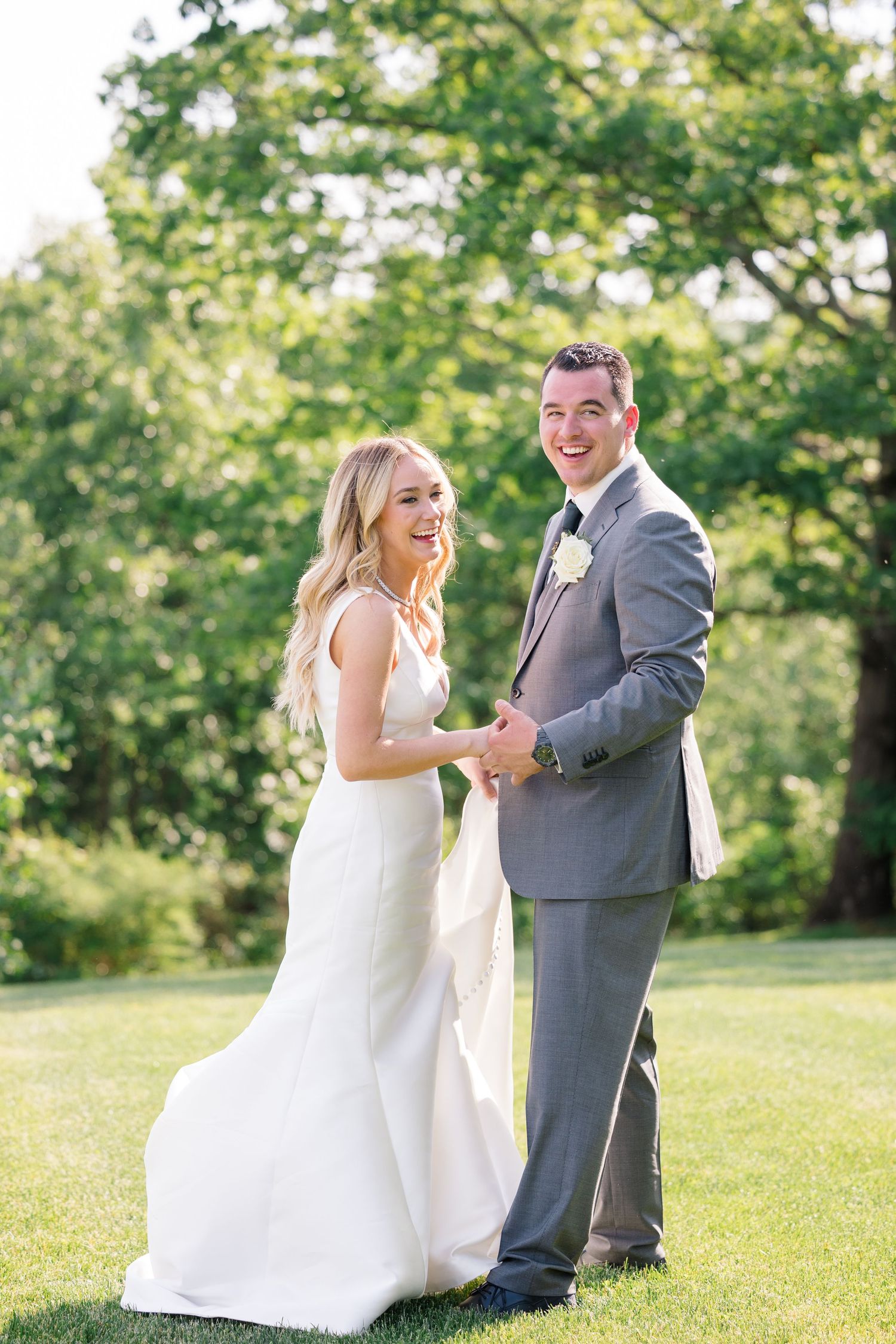 A candid moment of laughter between newlyweds on their wedding day in a garden setting.