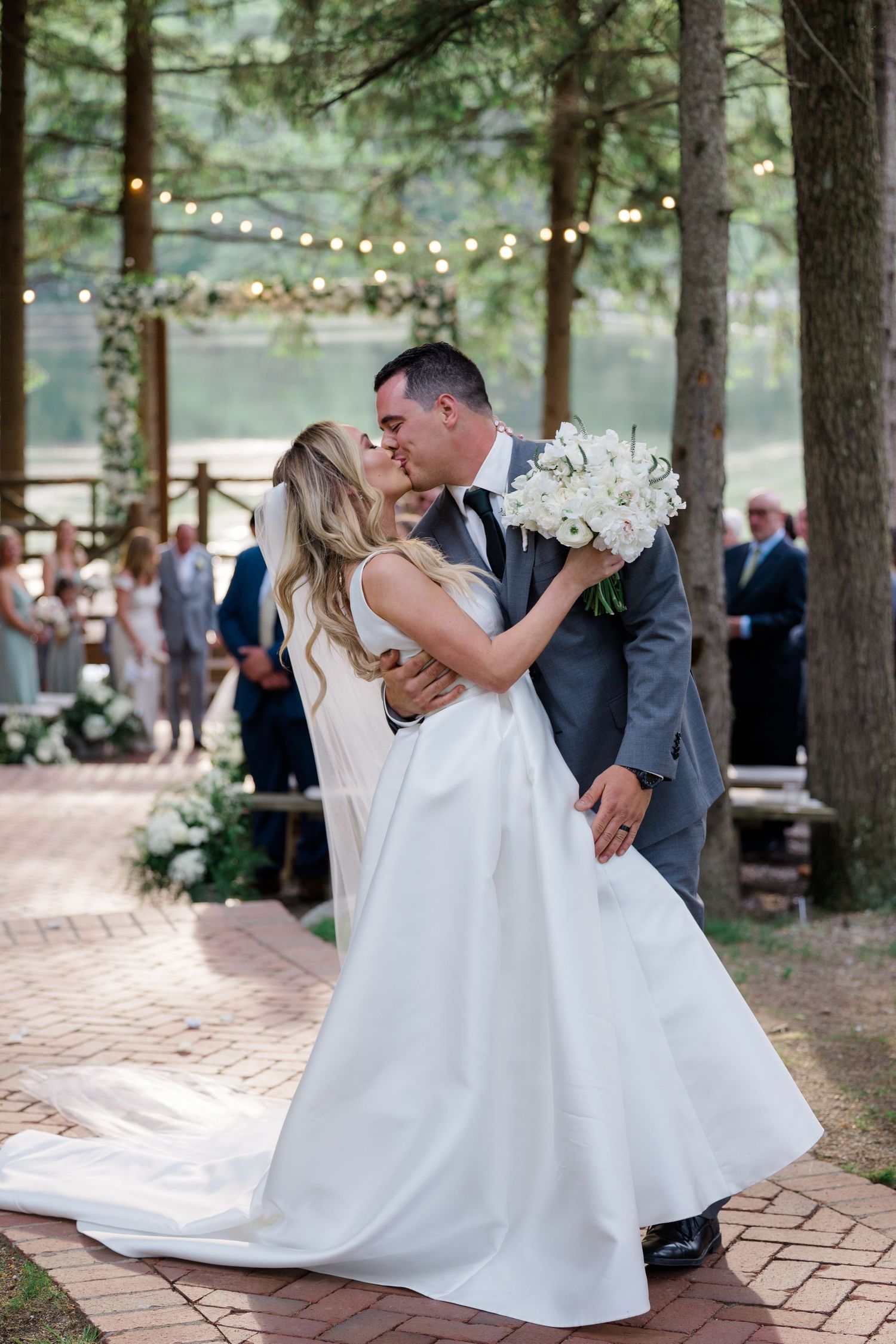 A romantic first dance moment at an outdoor woodland wedding with string lights and pine trees in the background.