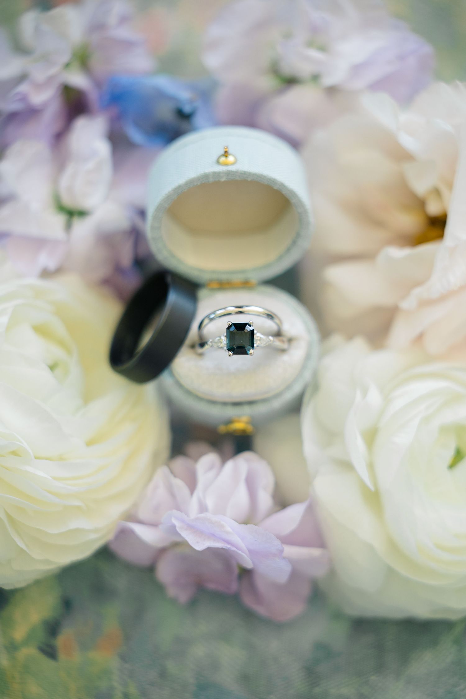 Elegant engagement ring nestled in a white box surrounded by soft white and purple flowers.